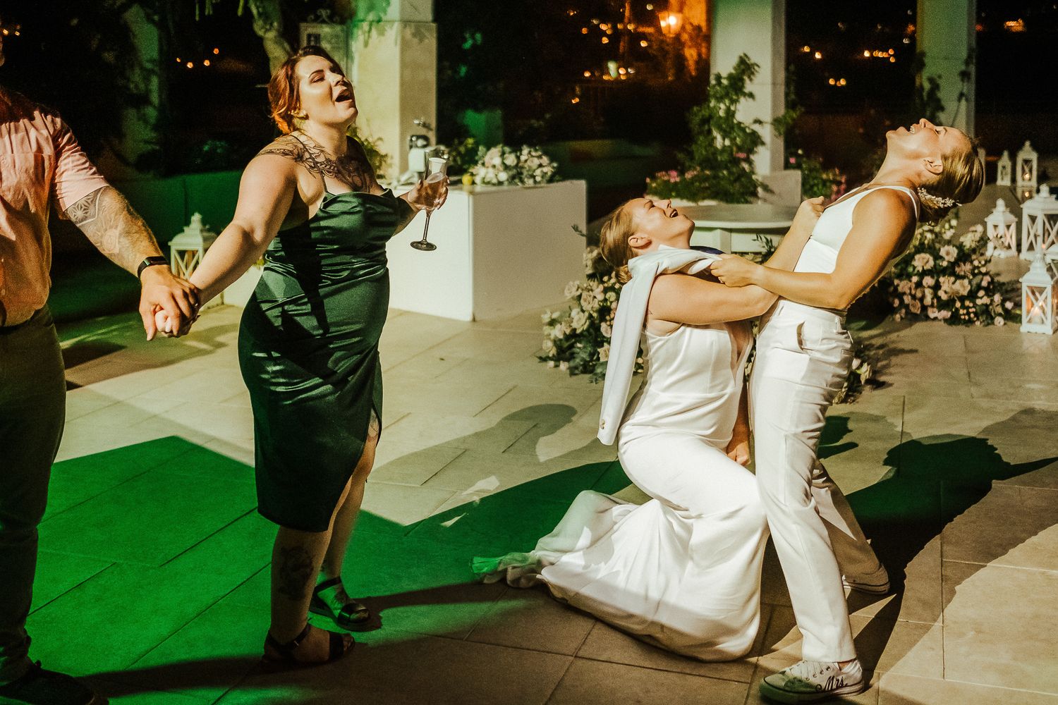 Wedding guests dancing and celebrating on an outdoor dance floor with green lighting.