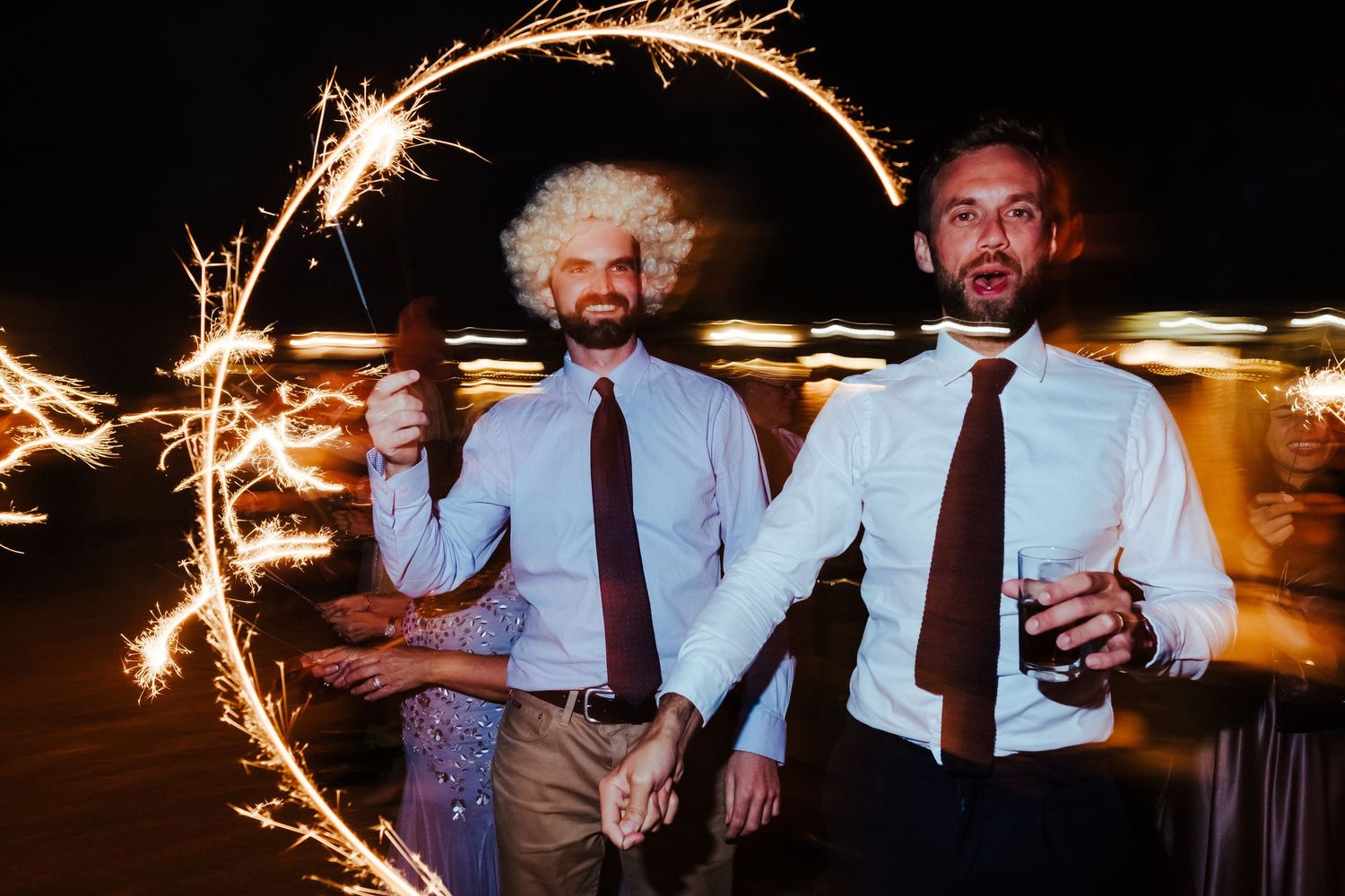 Two wedding guests pose with sparklers creating light trails in the dark.