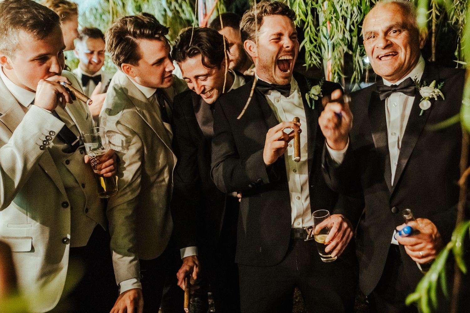Groomsmen share laughs and drinks during candid moment at wedding reception.