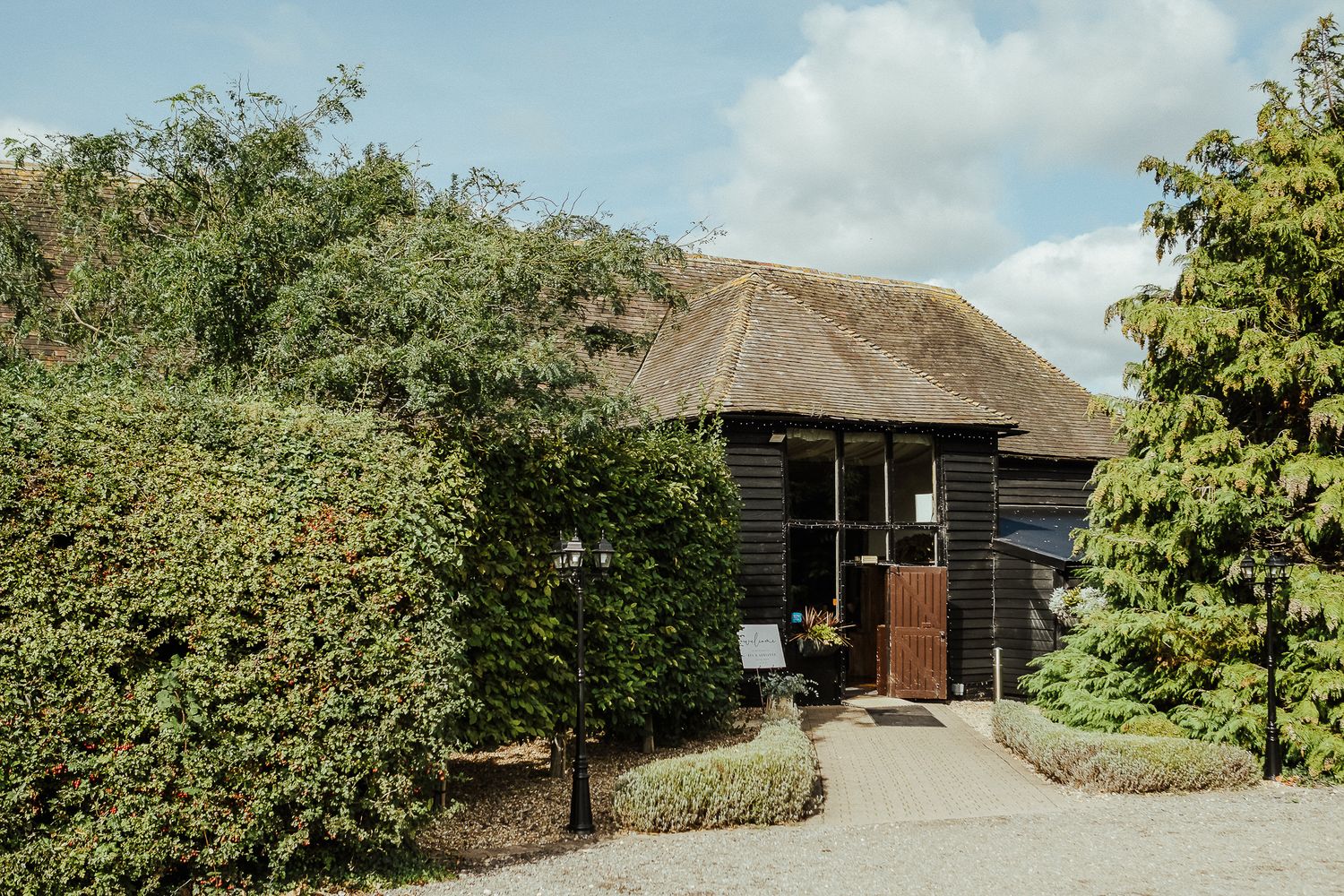 Rustic thatched-roof cottage with green hedges and blue sky.
