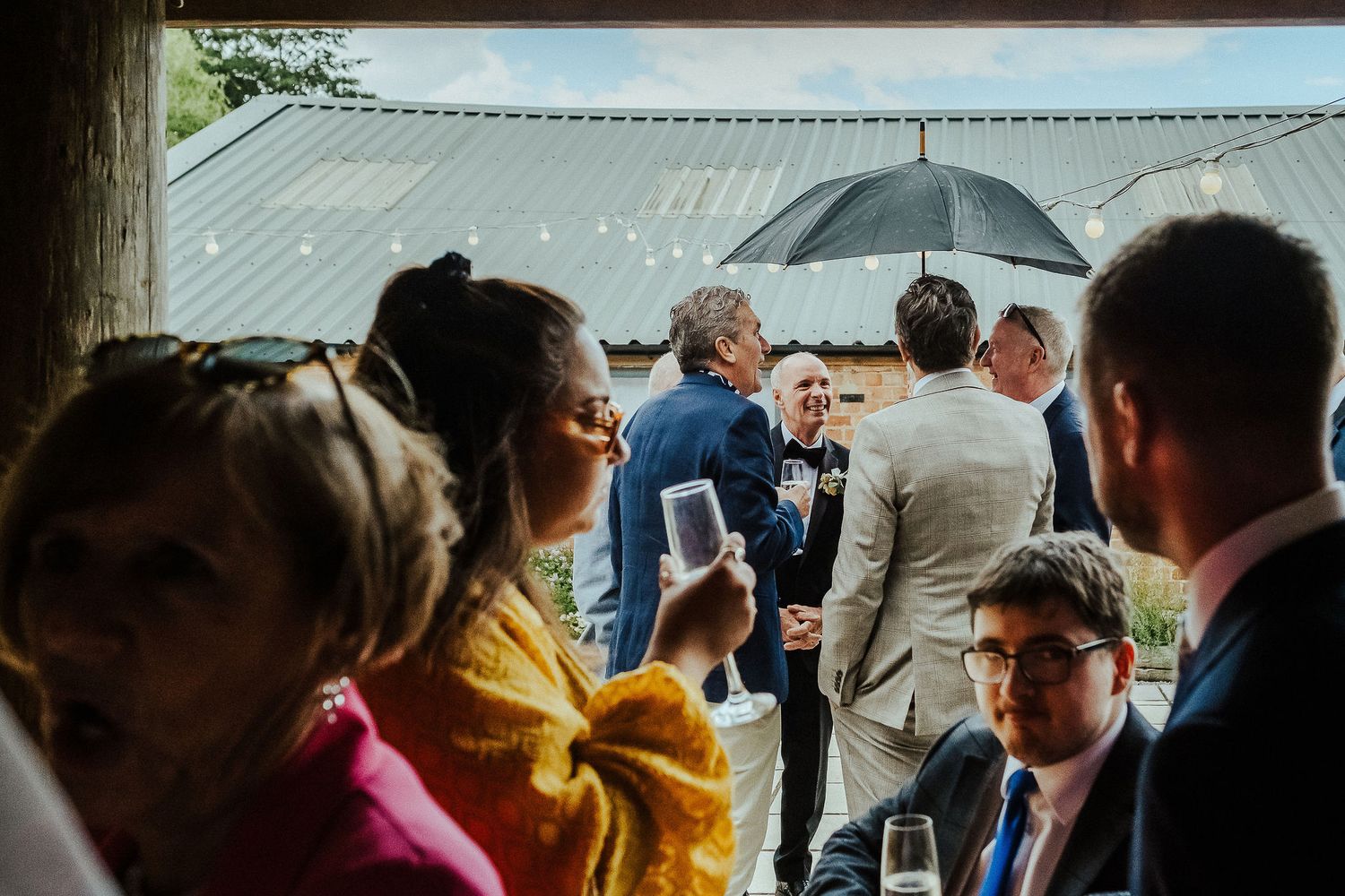 Wedding guests mingle and socialize during an outdoor reception under a covered patio.