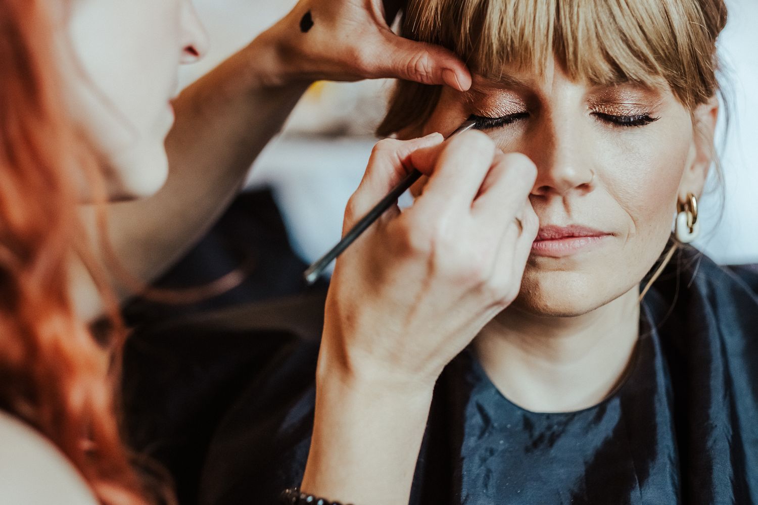 Close-up shot of makeup being applied with a fine brush during wedding preparations.