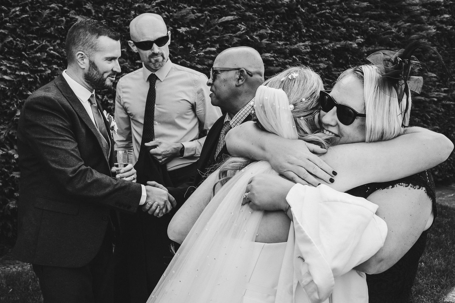 Black and white photo of emotional group hug at outdoor wedding celebration.