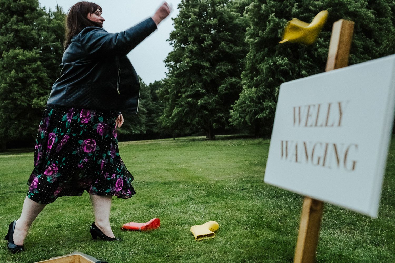 A guest plays welly wanging, an outdoor wedding game where participants throw rubber boots at a target.