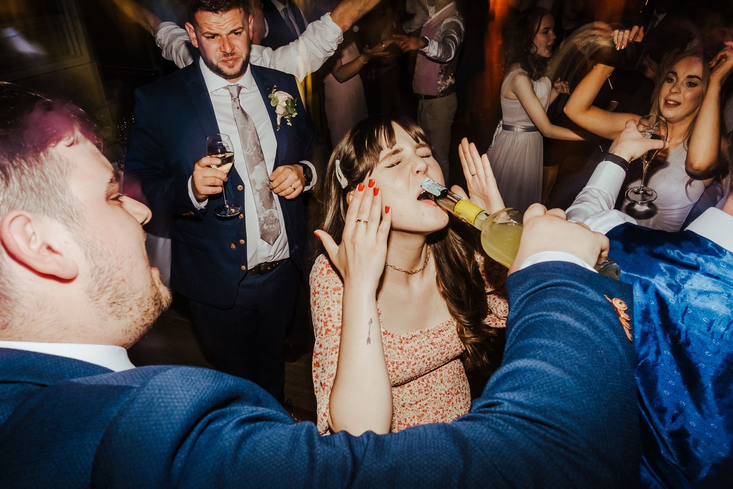 Wedding party guests dancing and celebrating on a dark dance floor with dramatic lighting.