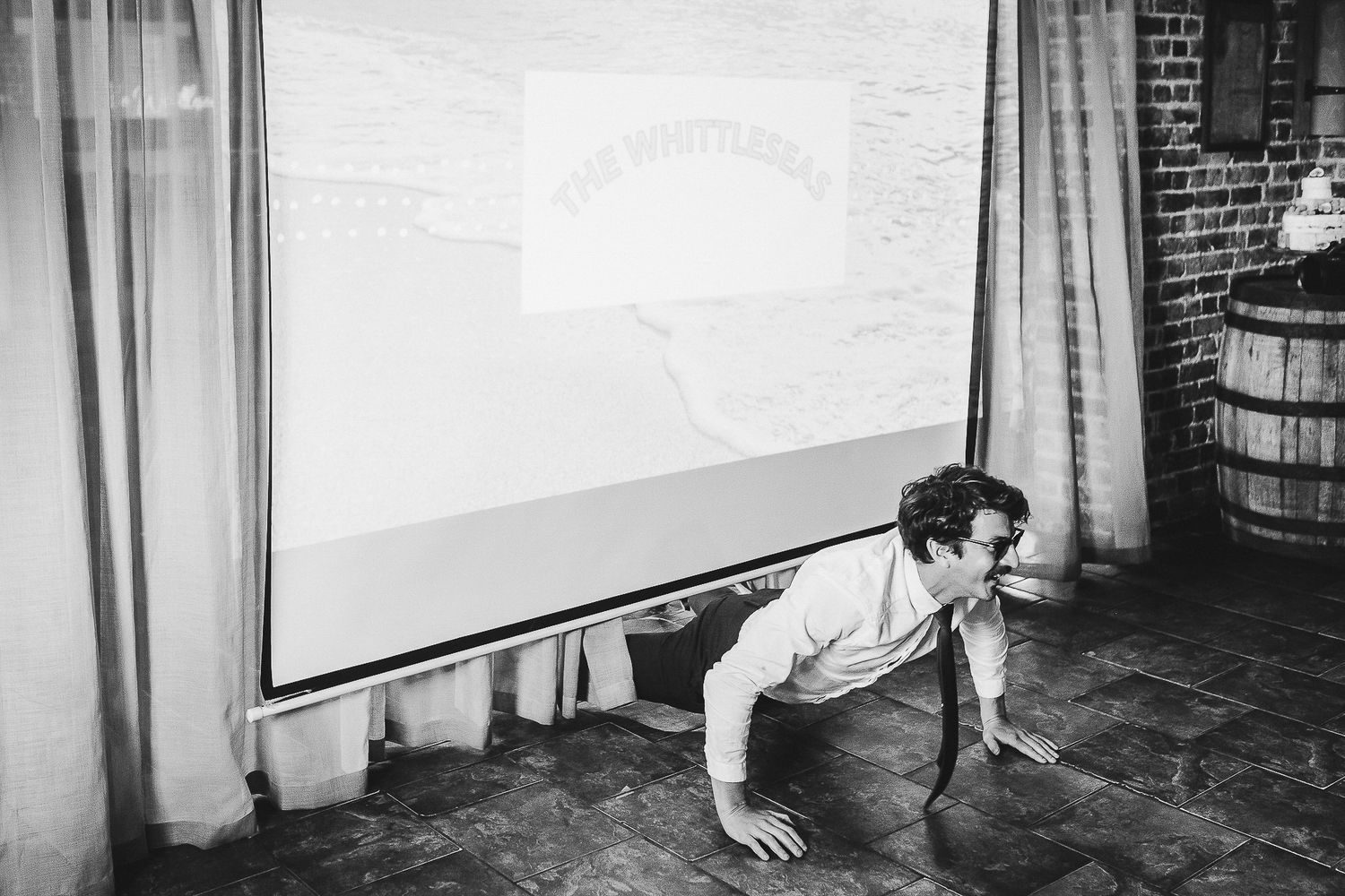 Black and white photo of someone performing an acrobatic move near a projection screen.