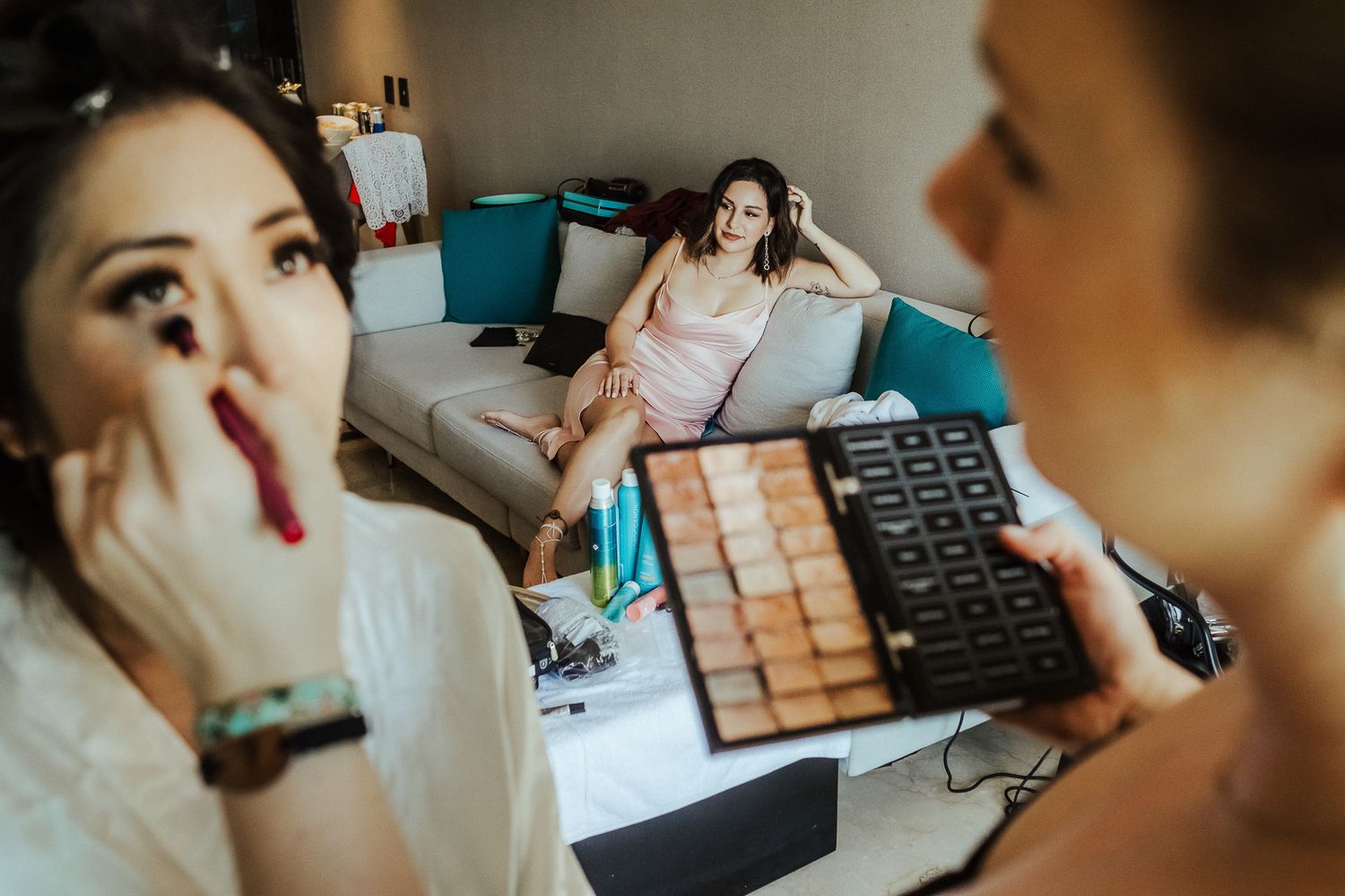Two people doing makeup preparation with a laptop on a bed.