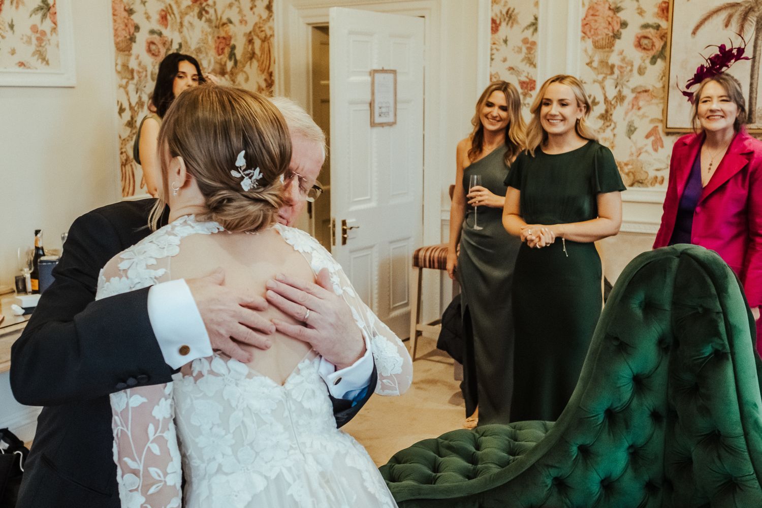 Wedding day preparations in a room with floral wallpaper and emerald green velvet furniture.