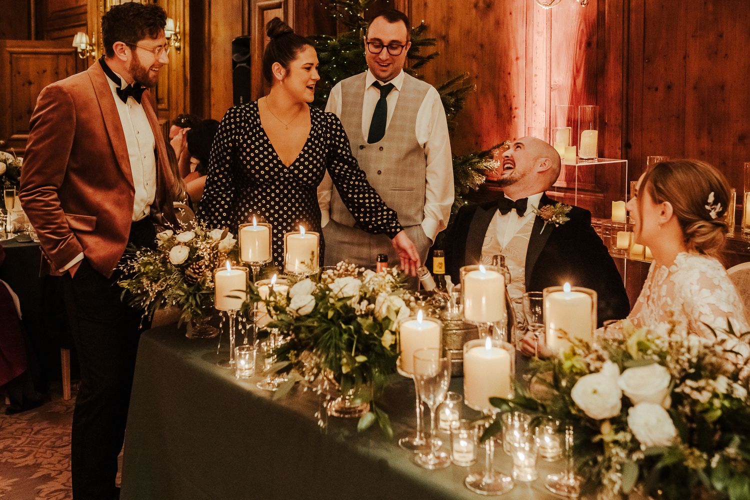 Wedding reception table decorated with glowing candles and lush greenery in rustic venue.