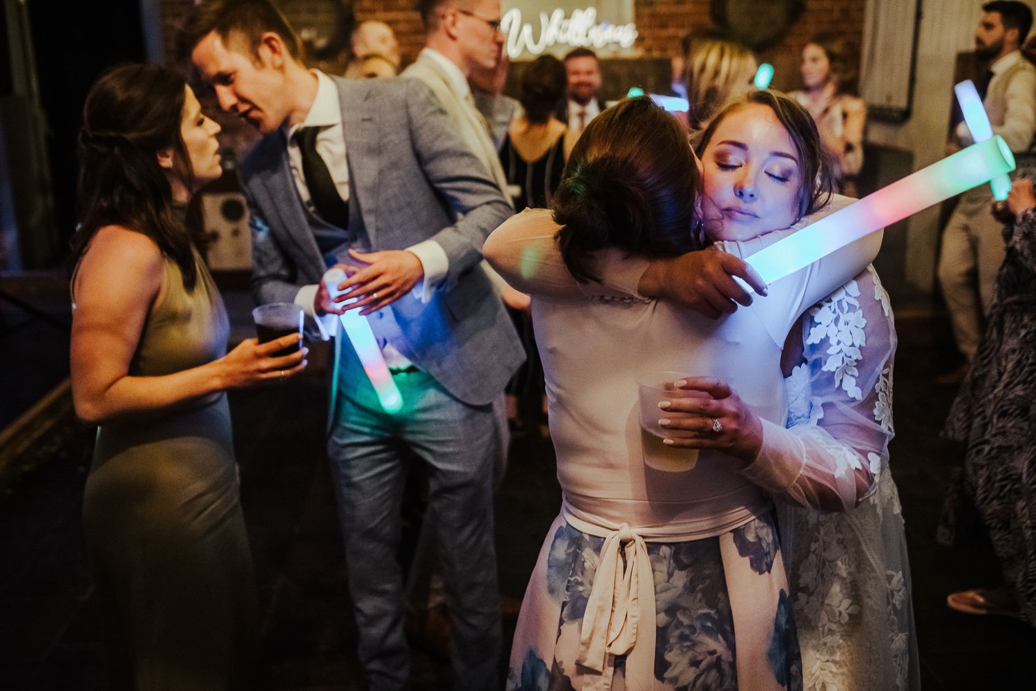 Celebratory dance party with guests waving colorful LED light sticks in a dark venue.