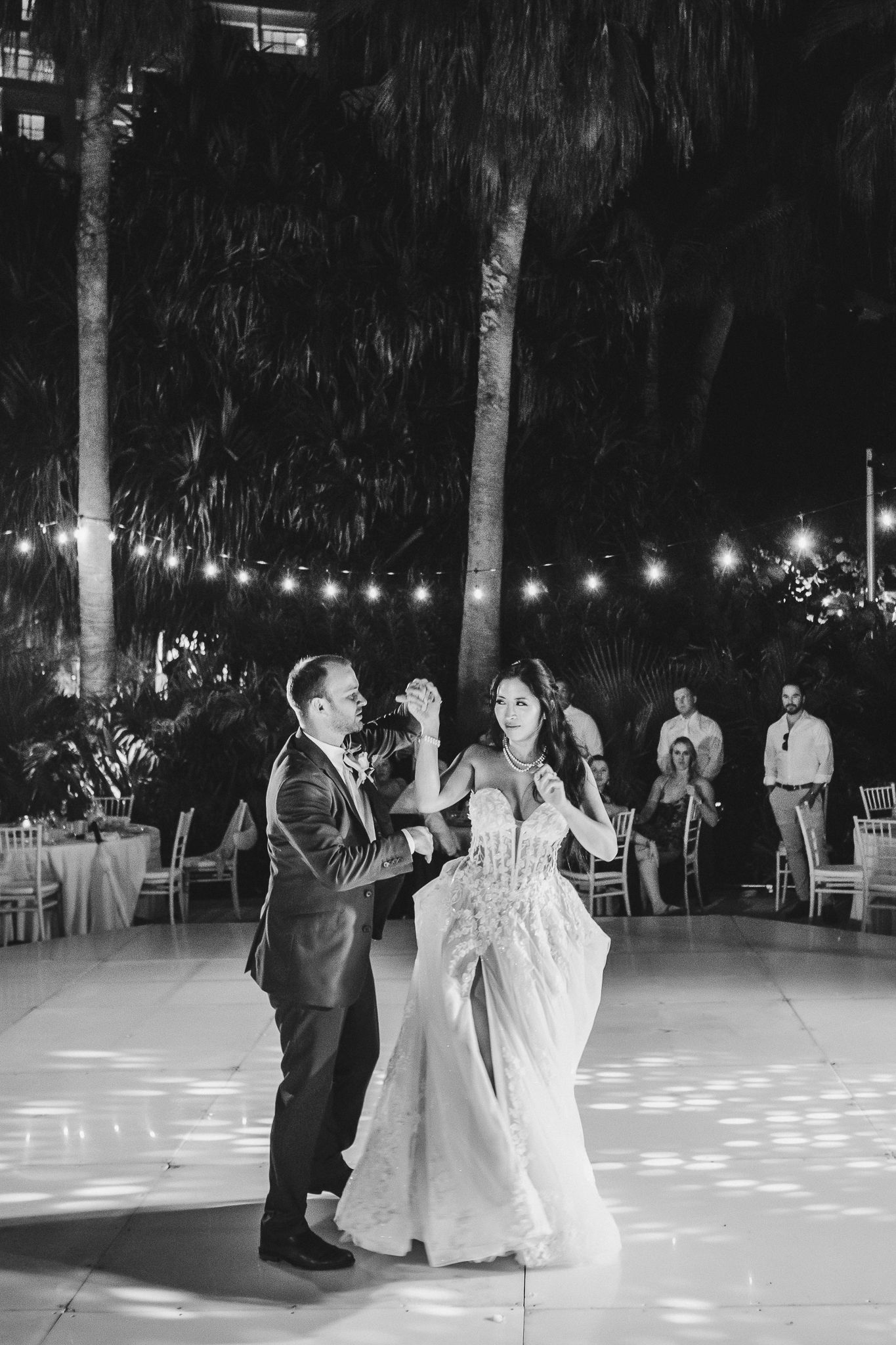 Black and white photo of couples dancing under string lights at an outdoor venue.