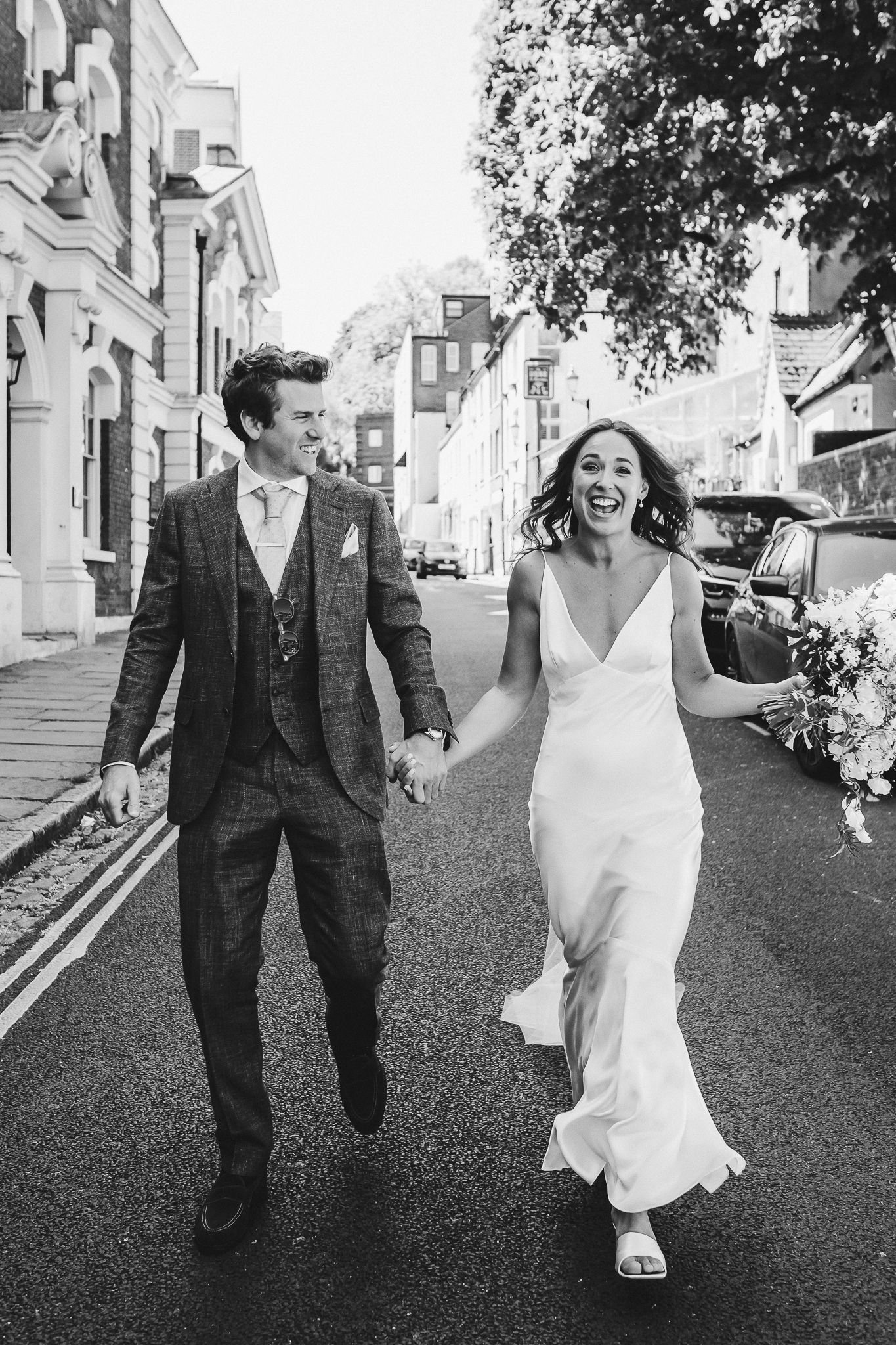 A black and white photo of a couple walking and laughing on a charming city street.