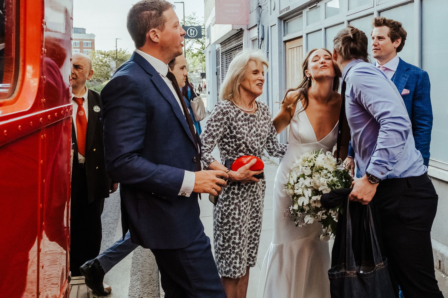 A celebratory moment beside a red vintage bus on an urban street.
