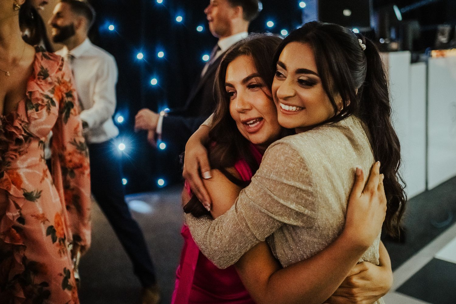 Two joyful people sharing a warm embrace while dancing at an evening event with twinkling lights in the background.