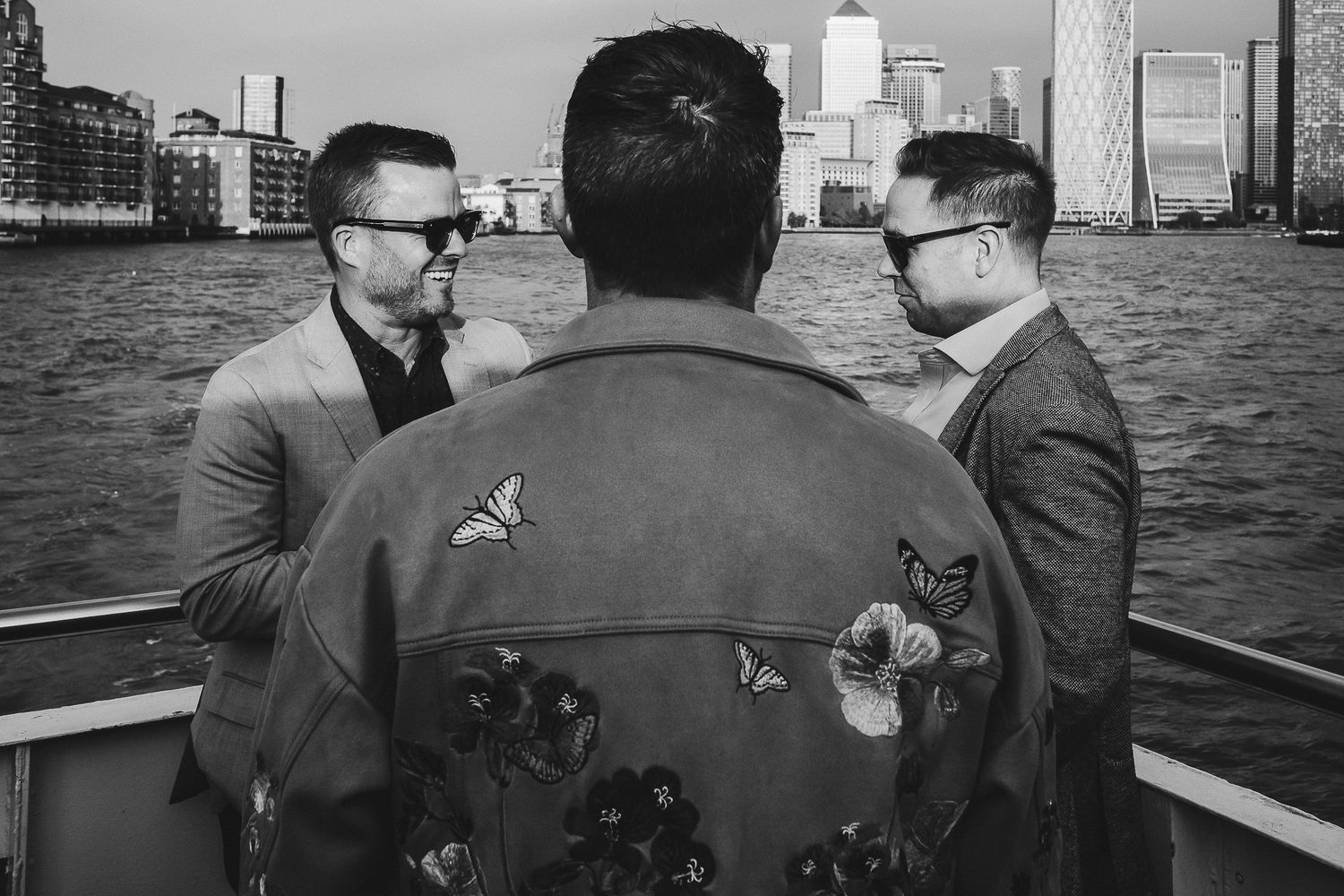 Three people having a conversation on a boat with a city skyline in the background.
