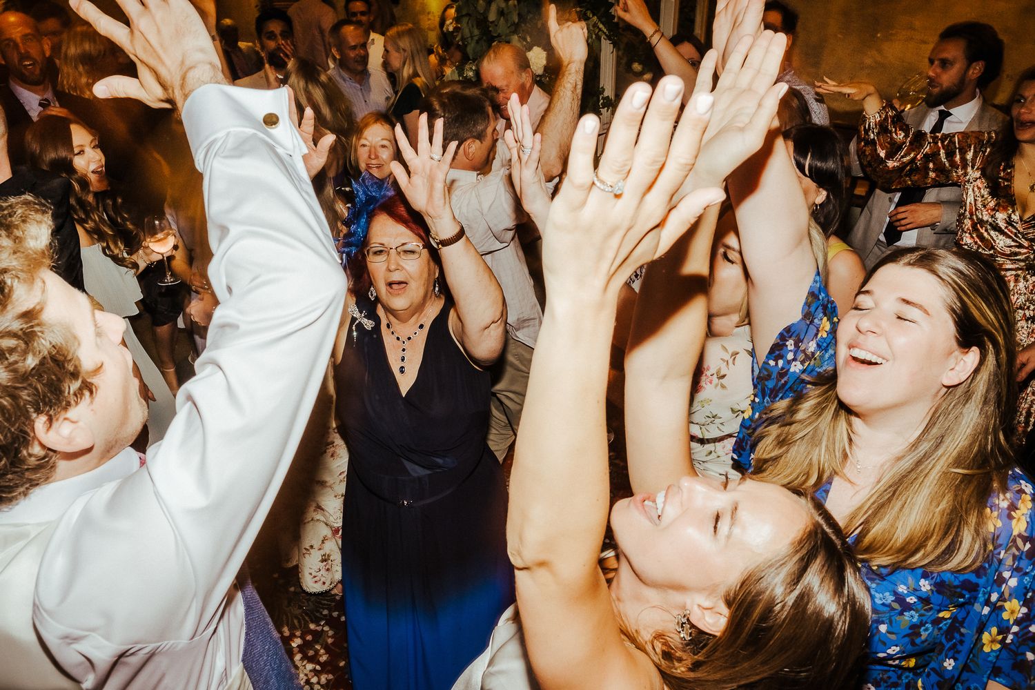 Enthusiastic wedding guests with raised arms dancing and celebrating on a packed dance floor.