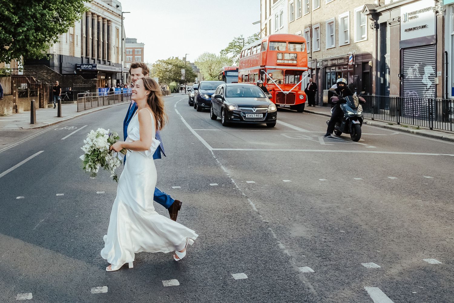 A white-dressed figure crossing a London street with a red double-decker bus in the background.