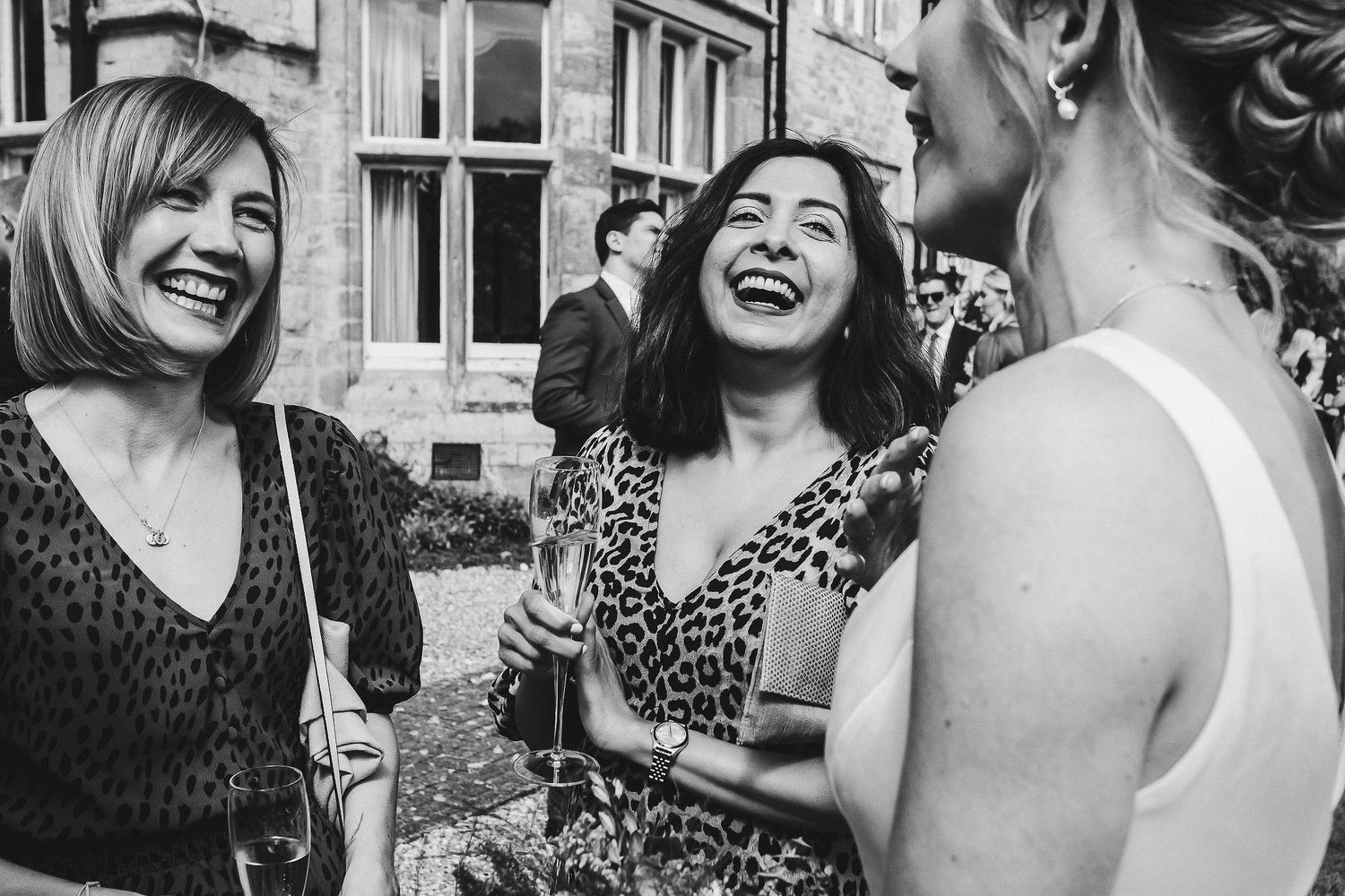 Black and white photo capturing spontaneous laughter between guests at outdoor wedding.