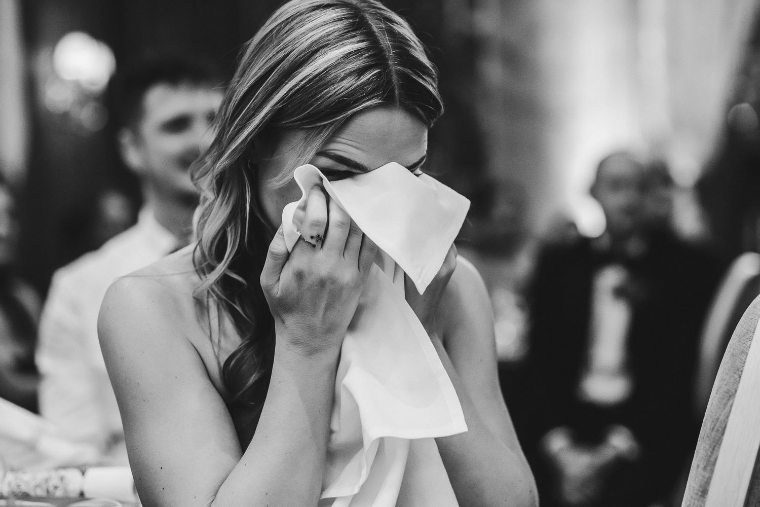 Emotional black and white photo of wedding guest wiping tears during reception.