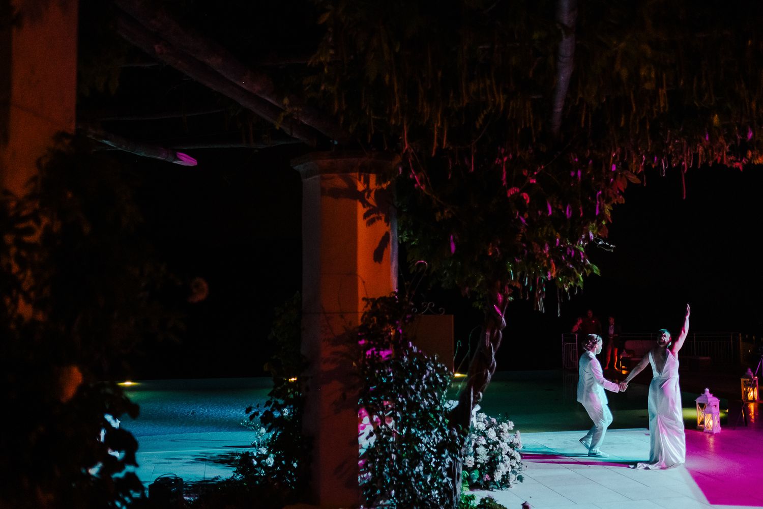 Artistic nighttime dance scene with colorful lighting and silhouetted figures at outdoor reception.