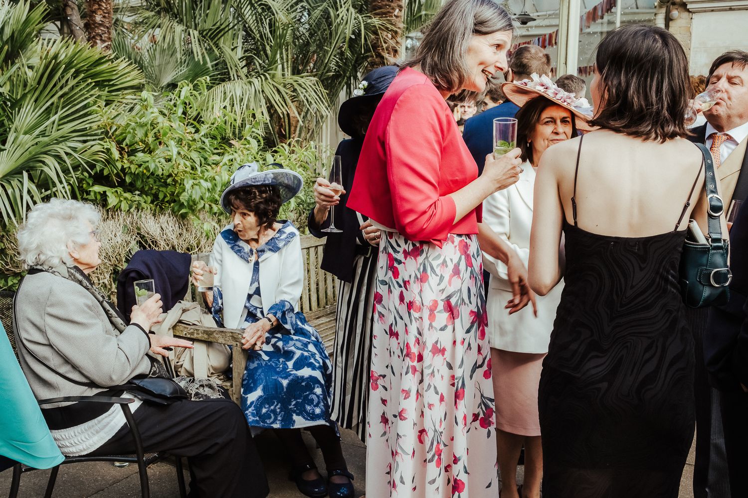Guests mingling at an outdoor garden wedding reception with tropical plants.