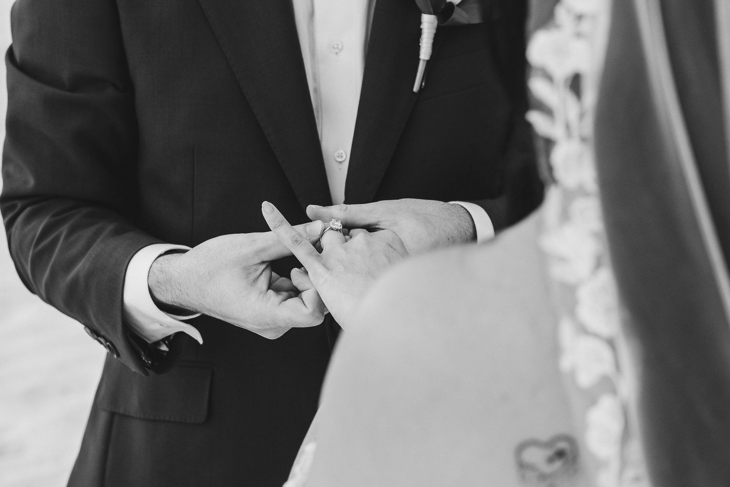 Close-up black and white shot of hands exchanging wedding rings during ceremony.