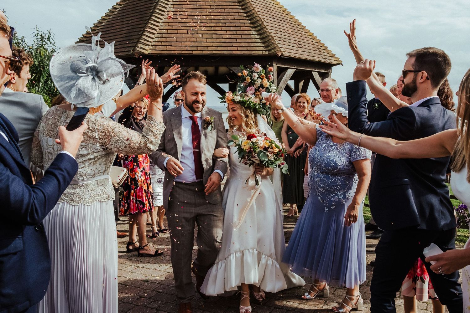 Celebration with wedding guests cheering and raising arms outside rustic venue.
