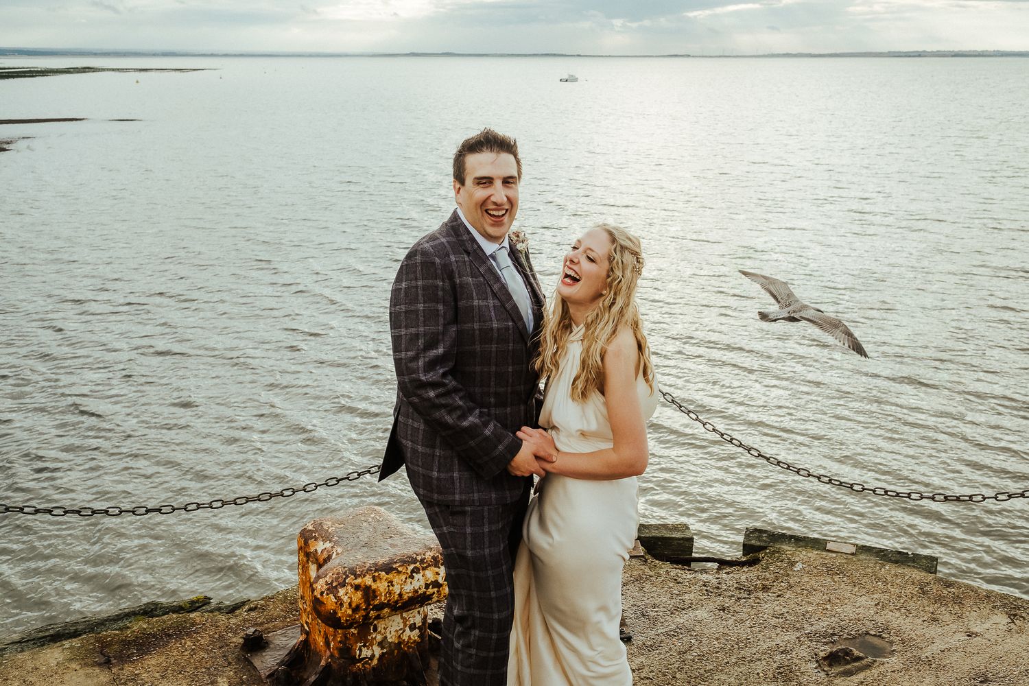 Romantic wedding couple embraces on a beach with scenic water views at sunset.