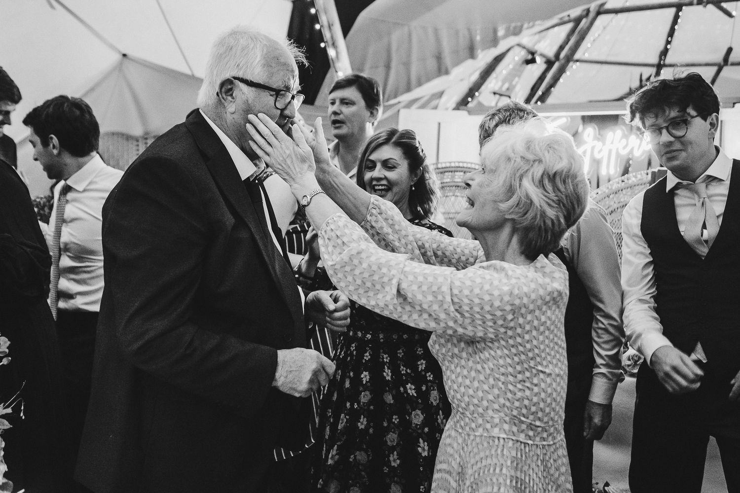 Wedding guests enjoying a lively dance moment under a tent.