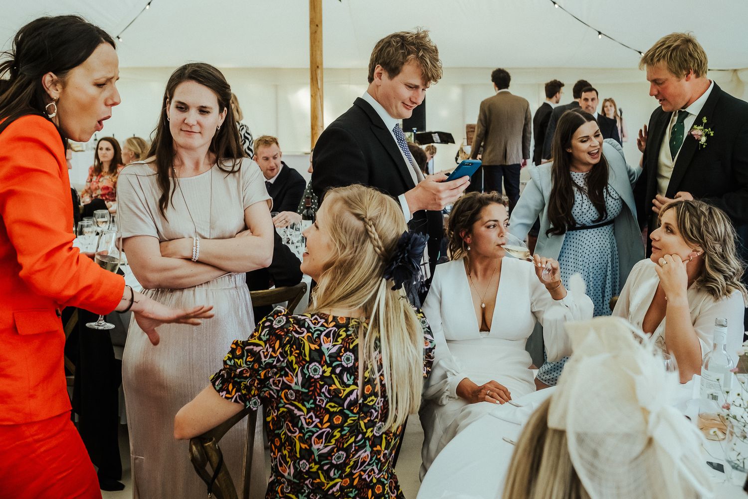 Wedding guests mingling and socializing during a daytime reception with string lights overhead.