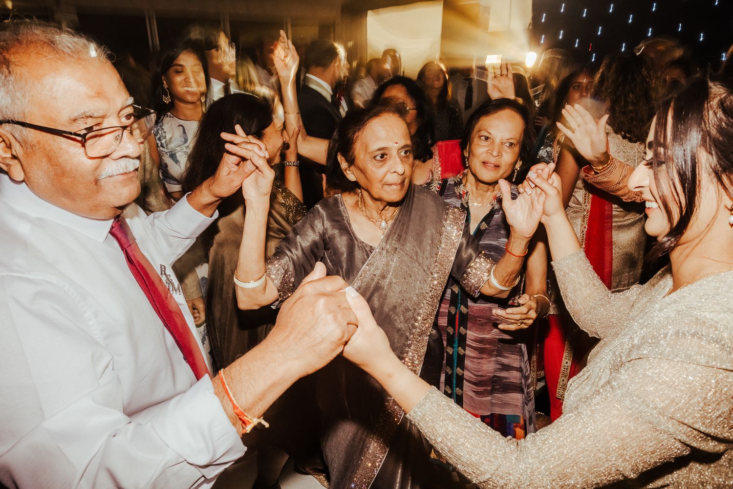 Party guests dance and celebrate together with joyful expressions in a dimly lit reception venue.