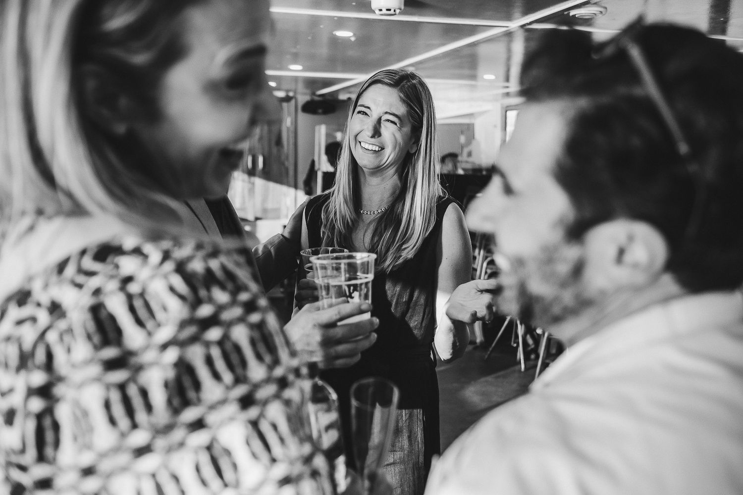 Friends enjoying drinks and conversation at a social gathering indoors in black and white photography.