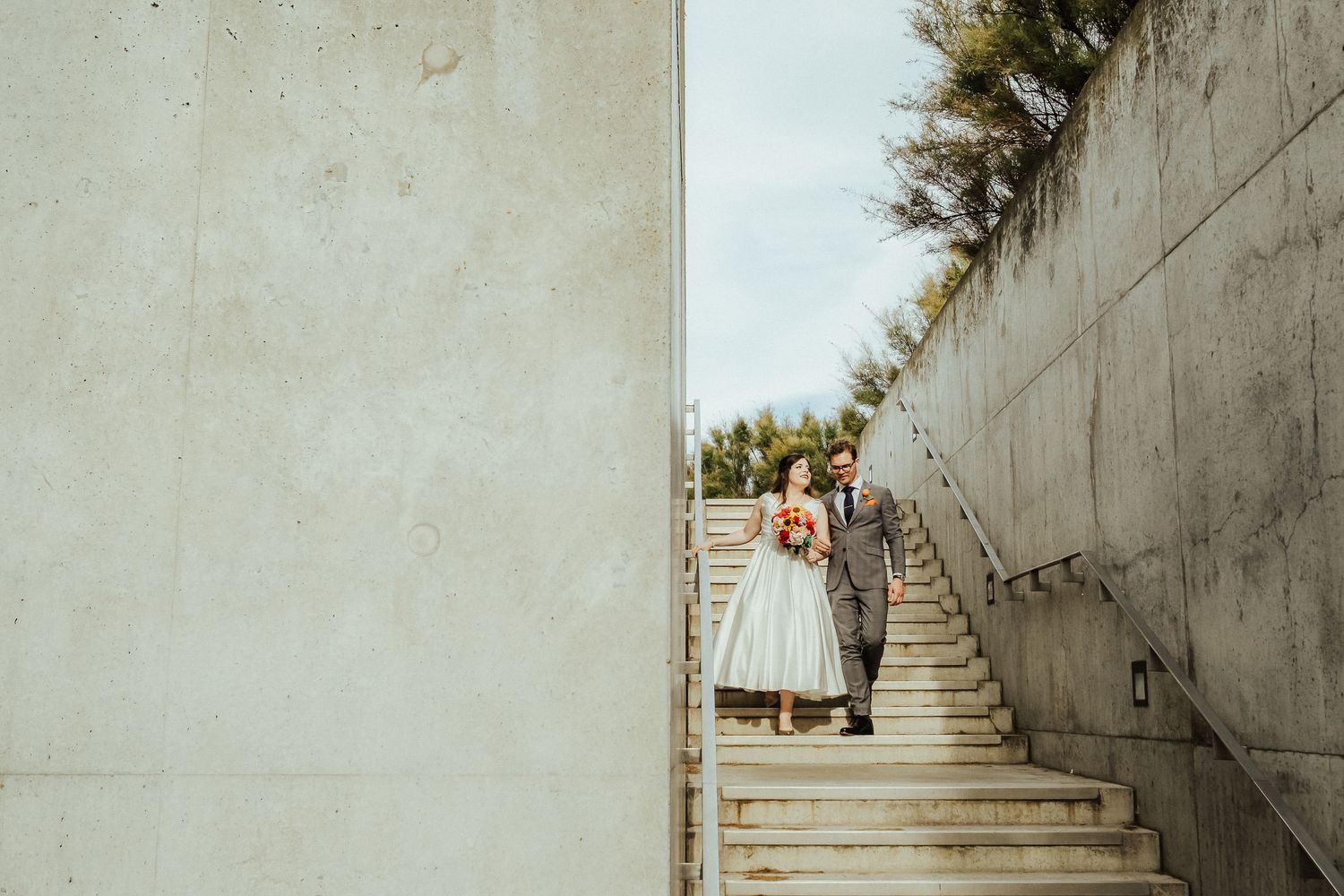 Tea-length wedding dress silhouetted on concrete steps with greenery above.