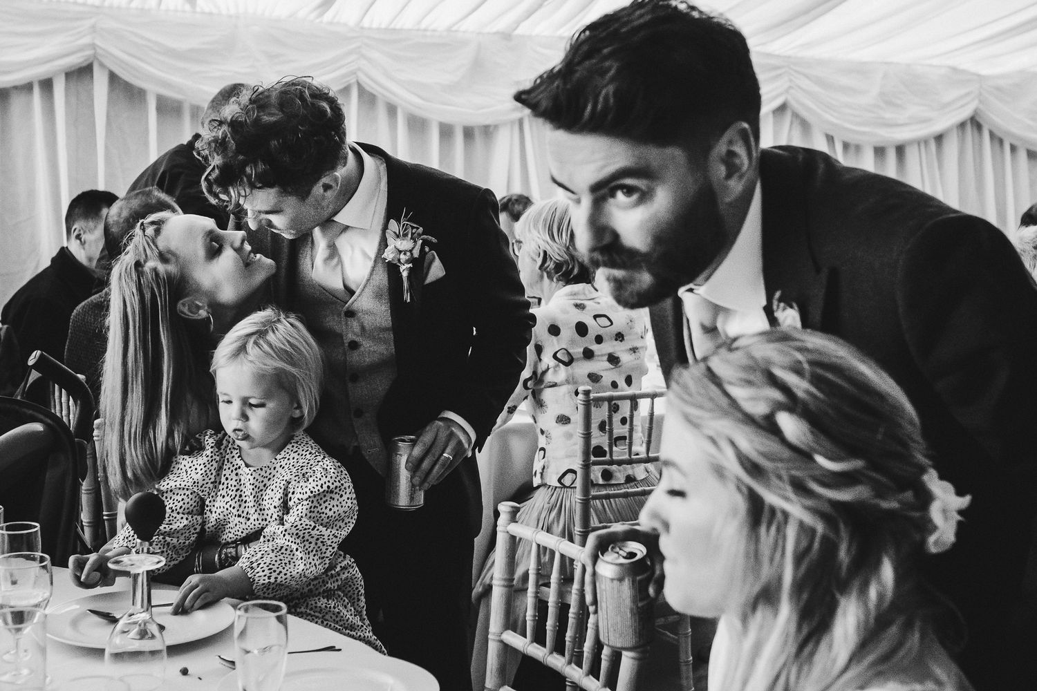 Black and white photo of wedding guests celebrating at a reception under a white tent.