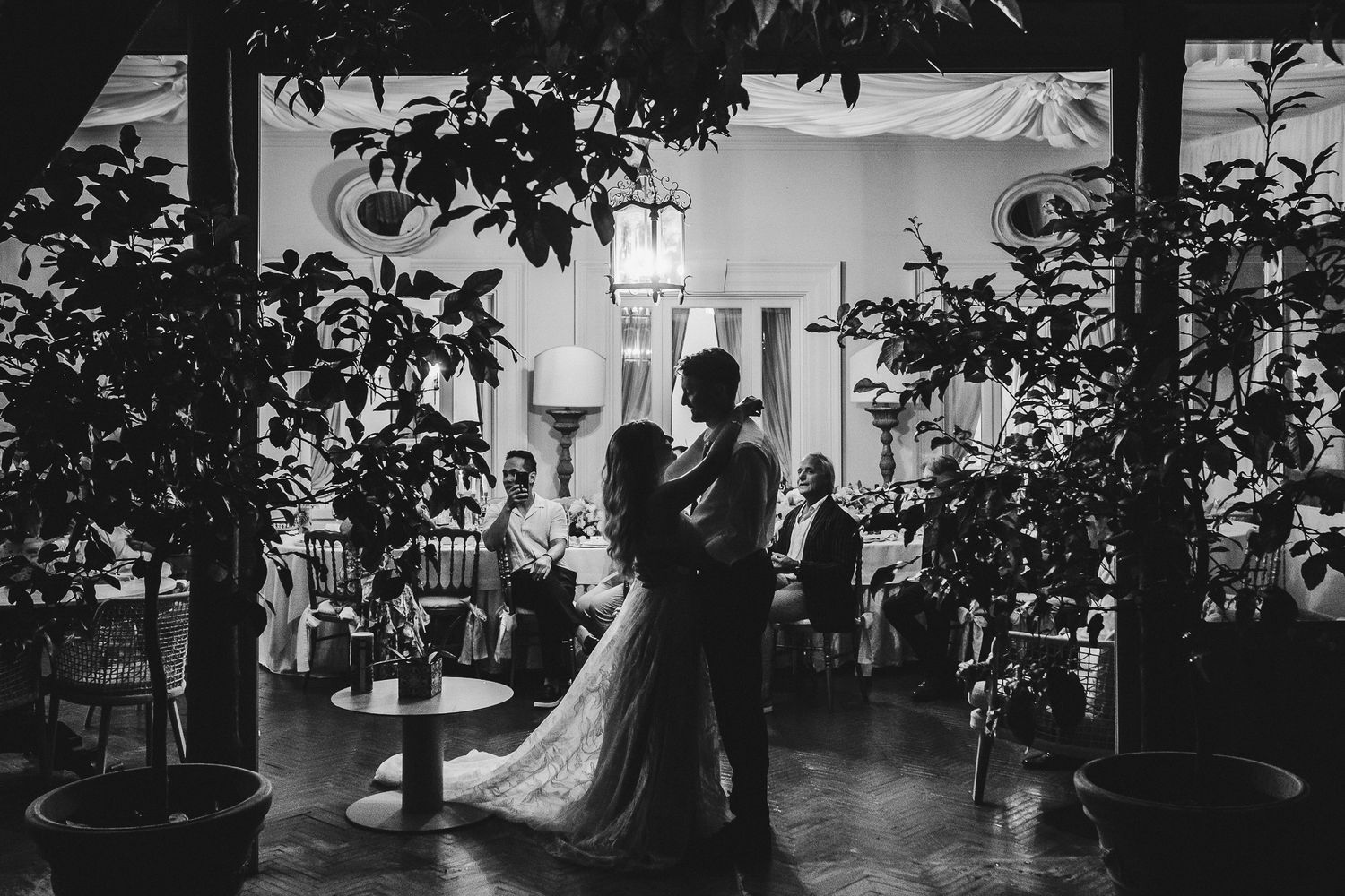 Silhouetted couple shares their first dance surrounded by indoor plants and ambient lighting.