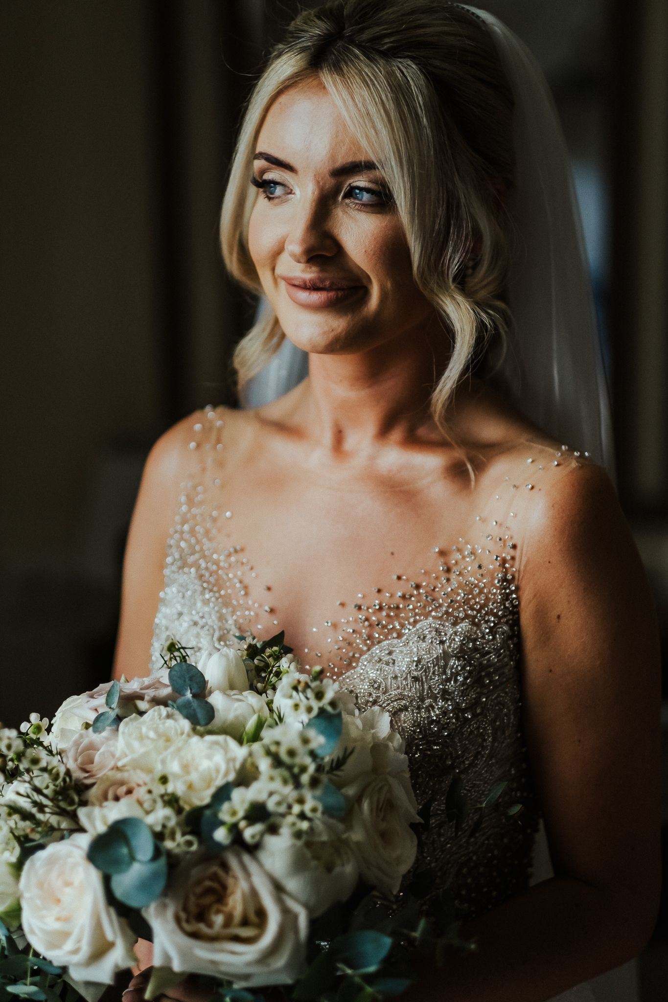 Bride in sparkly wedding dress holds white and blue bouquet while smiling.