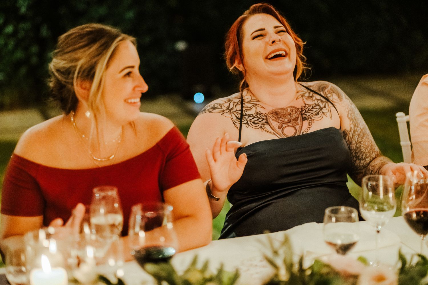 Two guests share genuine laughter during an outdoor evening reception.