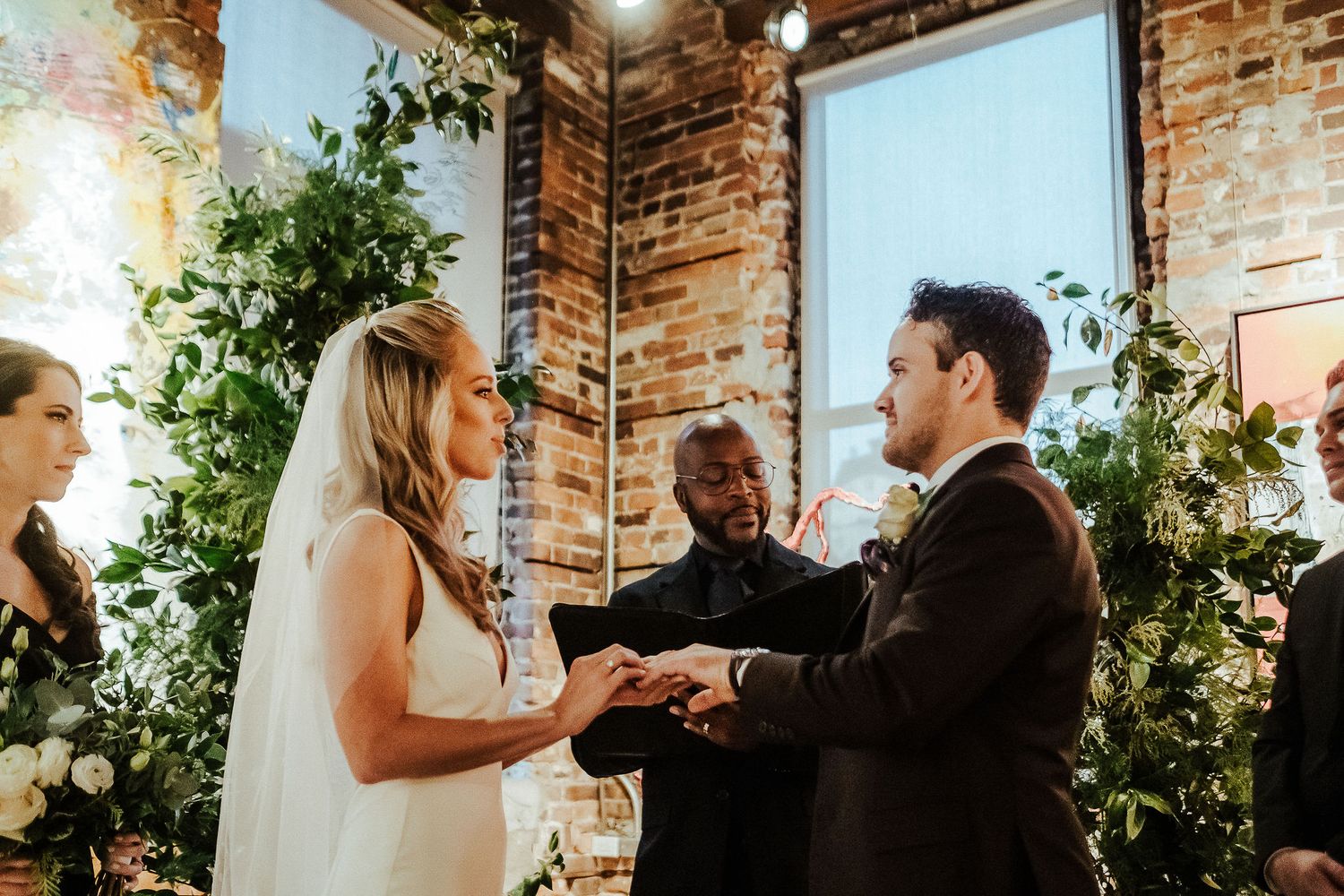 Couple exchanges vows in rustic brick venue with greenery decorations.