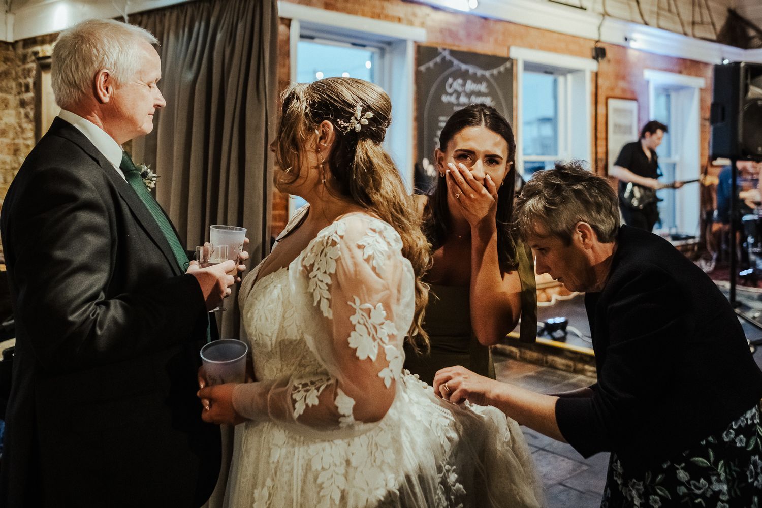 Intimate wedding scene with guests gathering around the bride in a cozy indoor setting.
