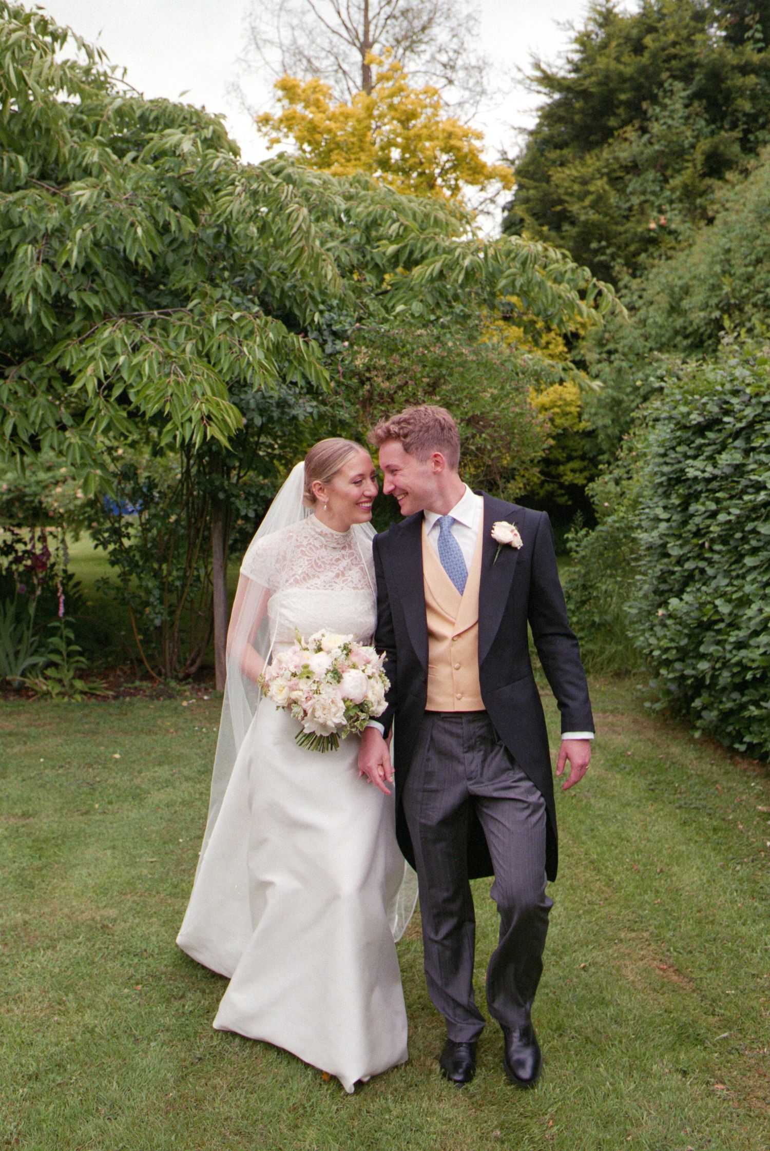 Newlywed couple walking together through a beautiful garden setting on their wedding day in natural sunlight.