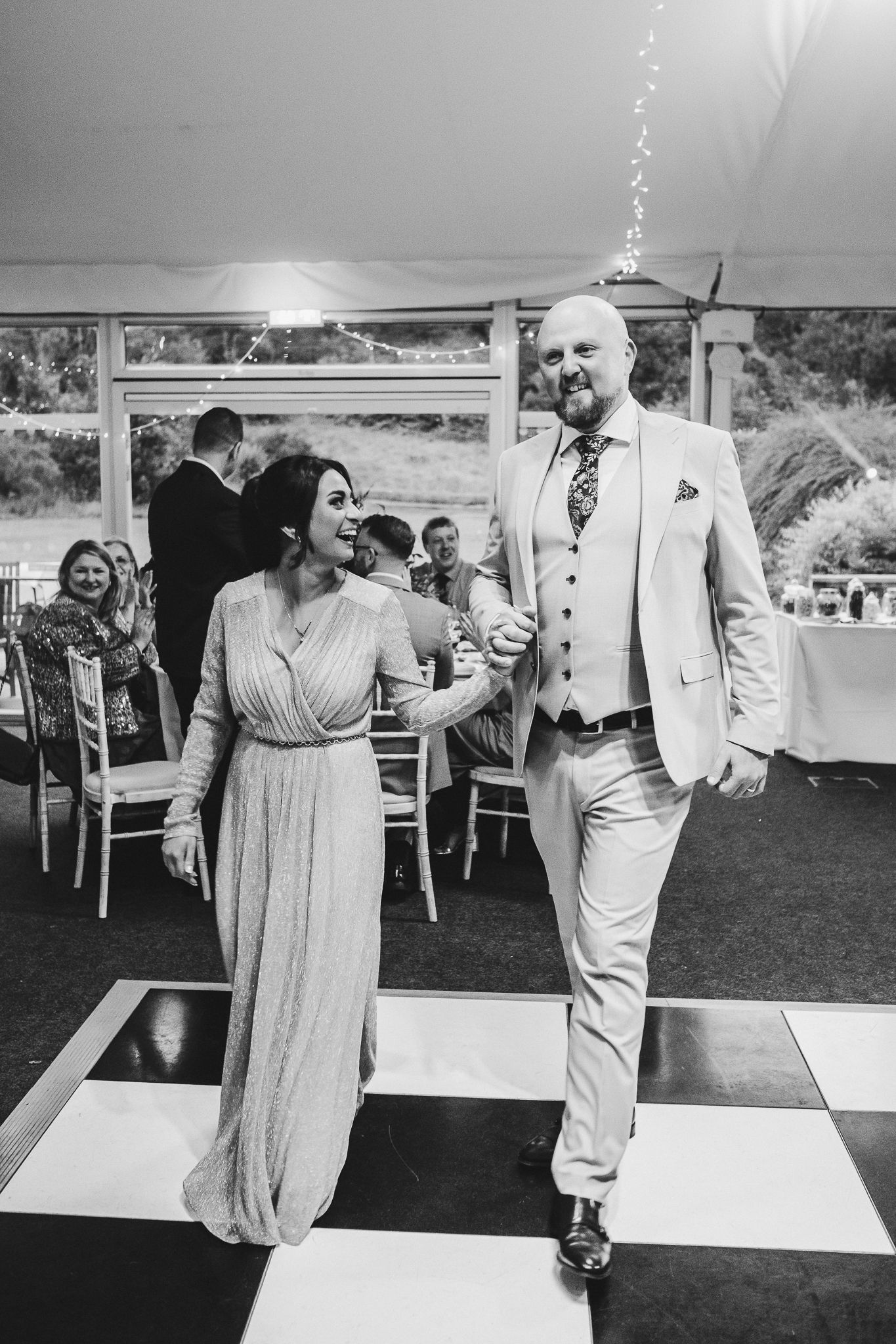 A joyful dancing moment captured in black and white on a checkerboard dance floor at an outdoor wedding reception.