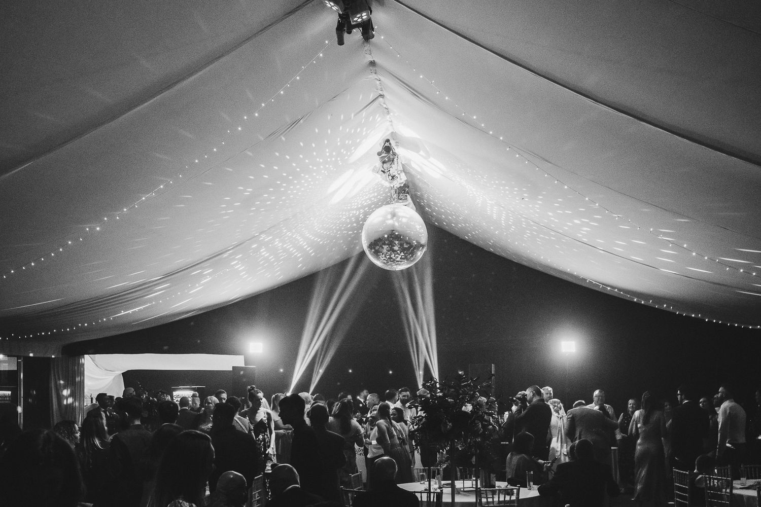 Black and white photos showing a tented wedding reception with disco ball and dance floor decorated in elegant style.