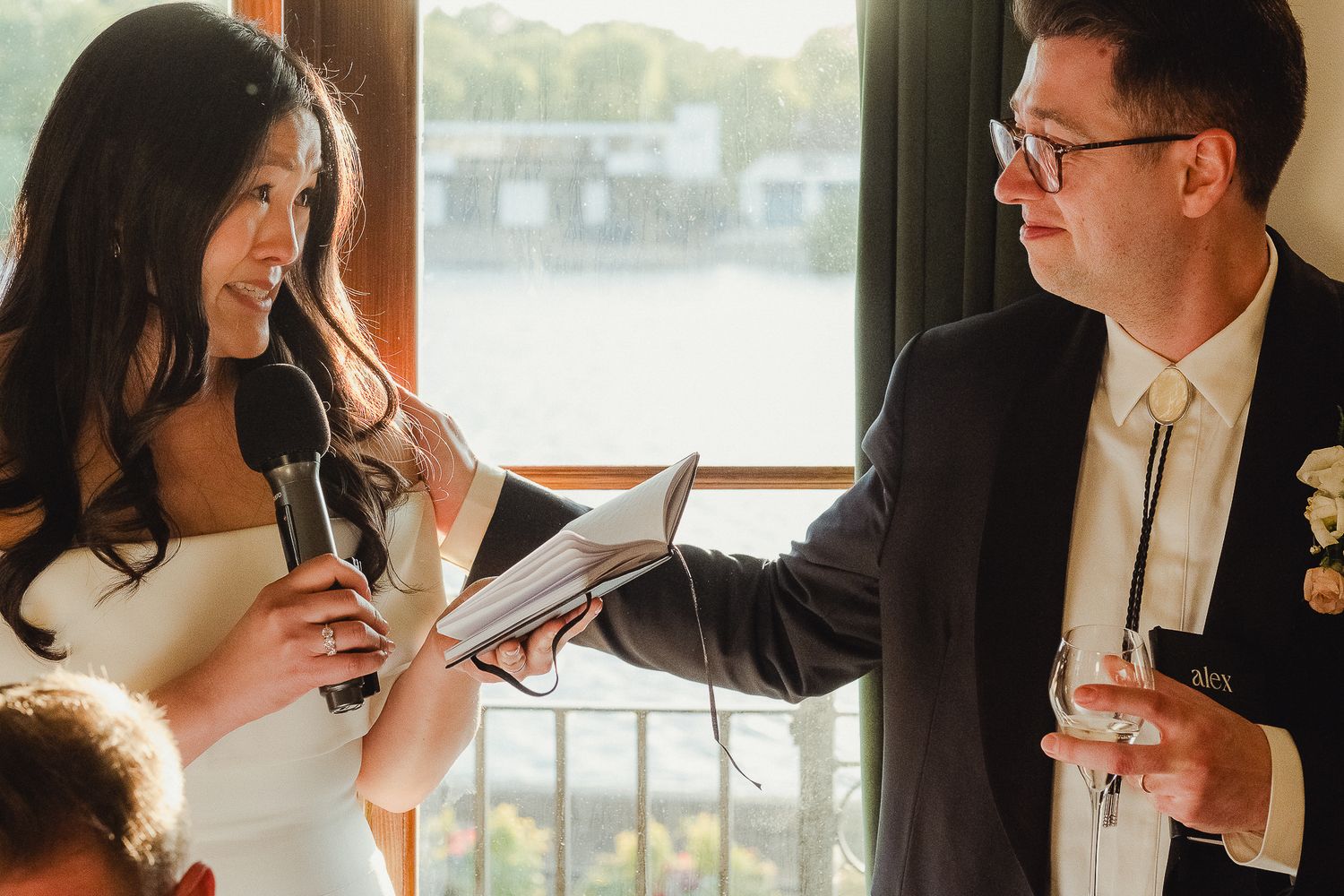 Romantic couple striking affectionate poses for wedding photos beside bright windows in elegant formal attire.