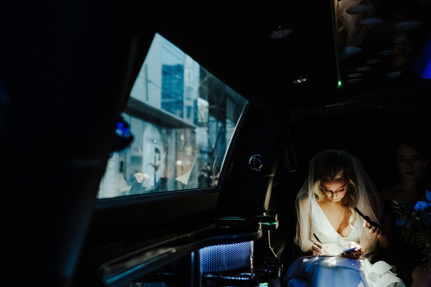 Bride checking phone in backseat of car at night with blue lighting.