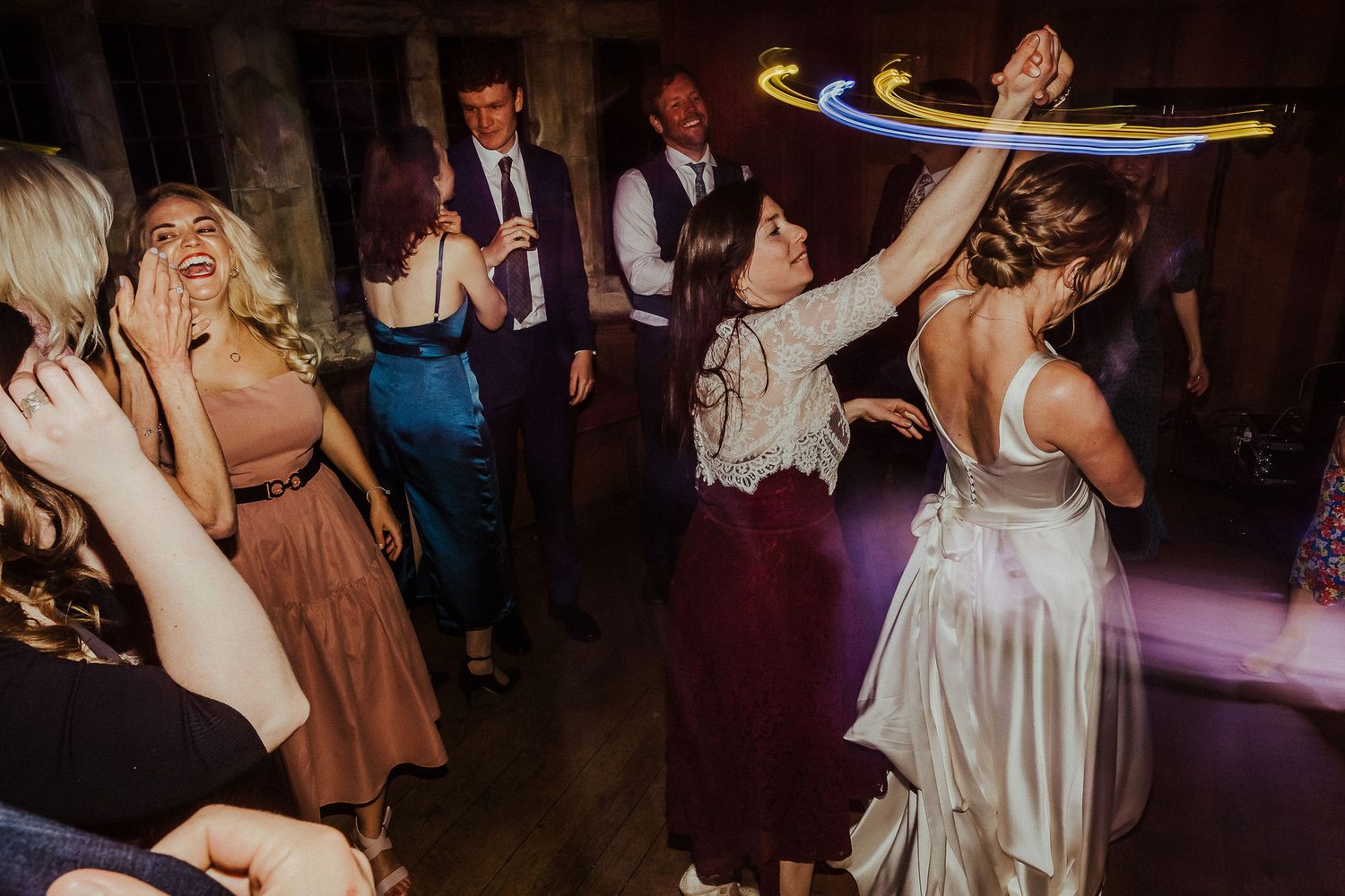 Wedding guests dancing and celebrating with glowsticks on a dimly lit dance floor.