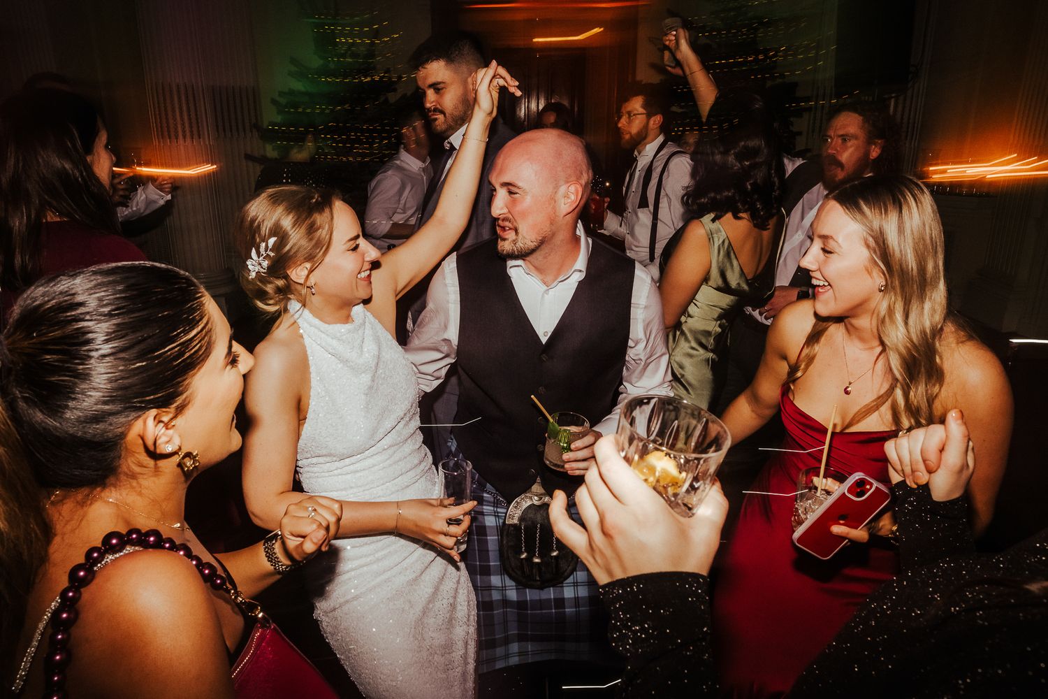 Wedding reception dance floor filled with guests under moody atmospheric lighting.