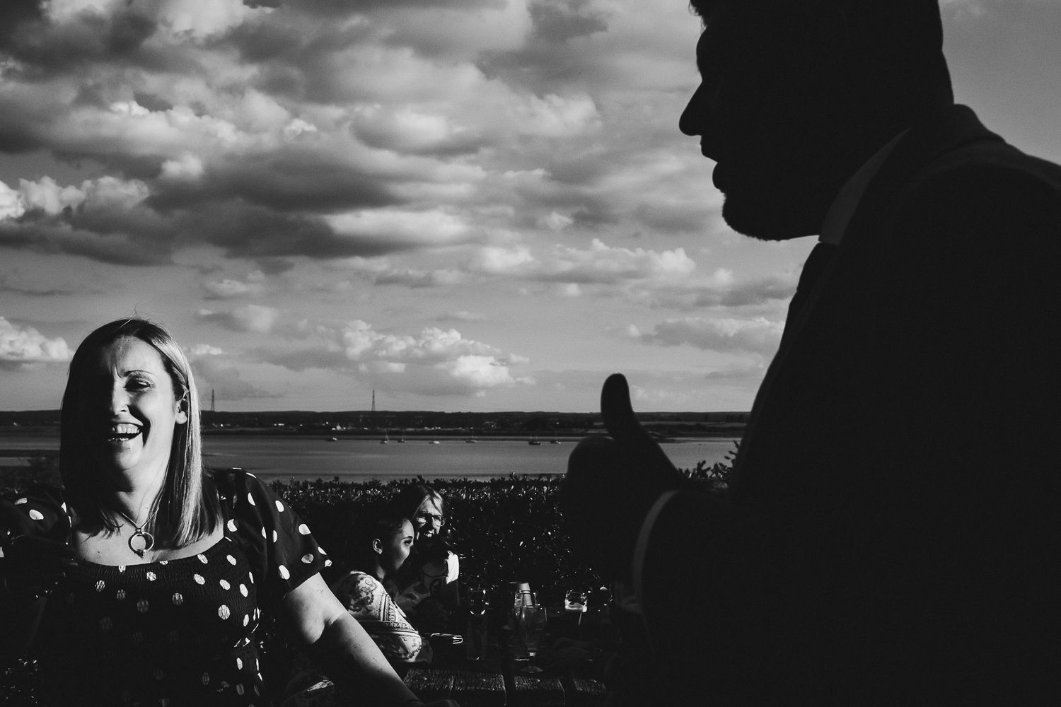 A candid black and white photo of guests enjoying an outdoor reception by the water.