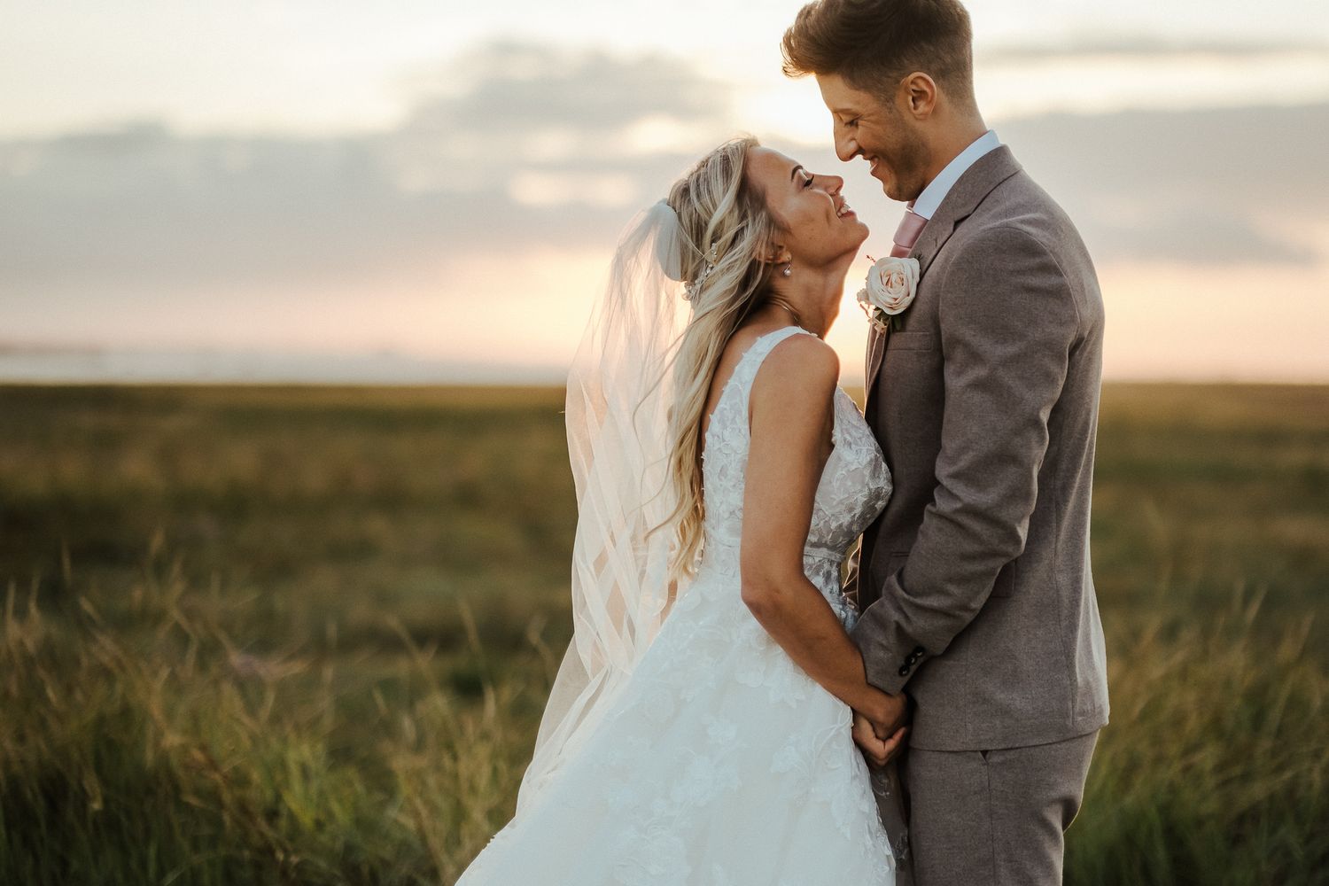 Couple embracing in golden sunset light against rural landscape backdrop.