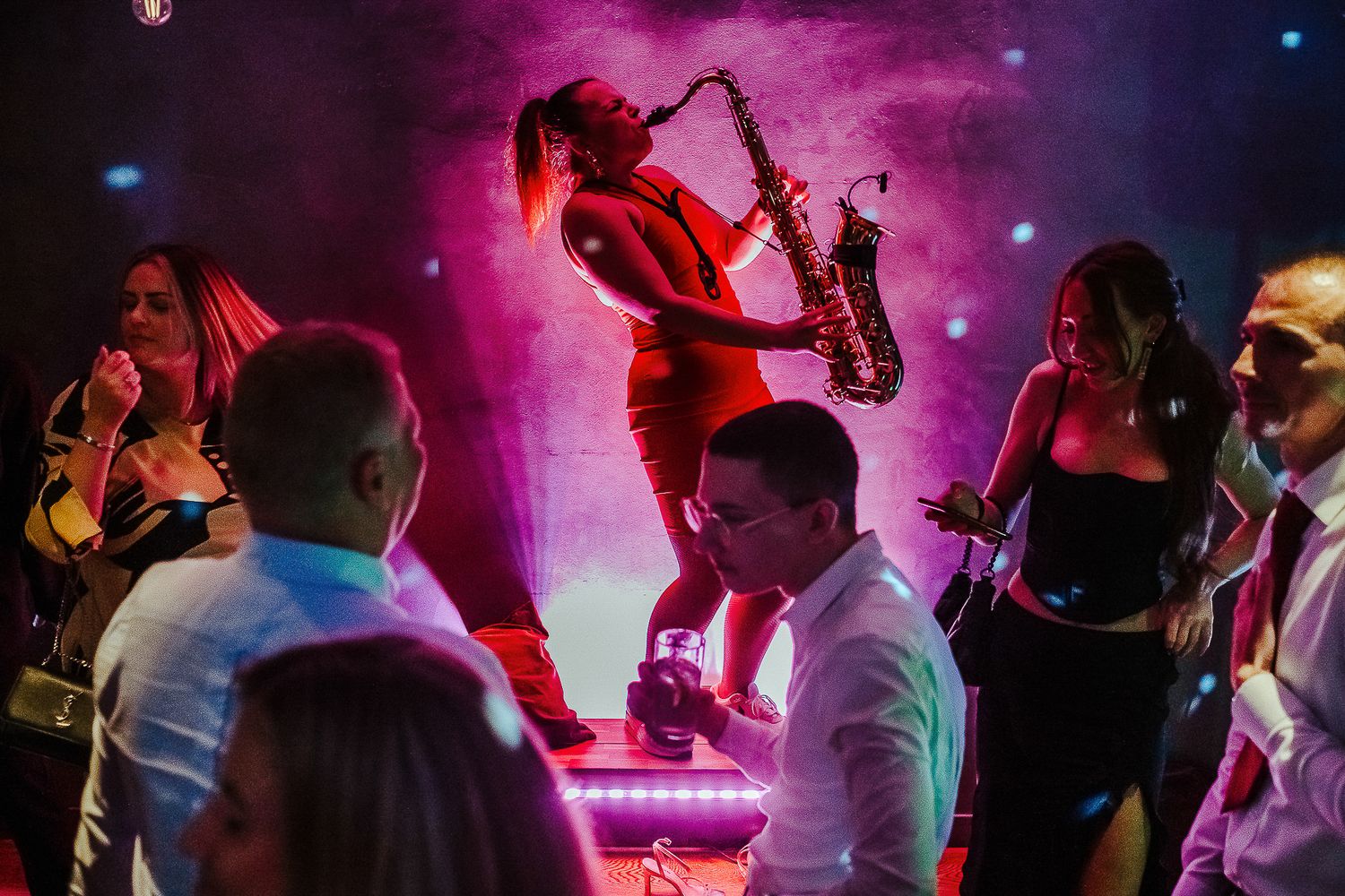 Saxophone player performing on stage with dramatic purple lighting at a live music event.