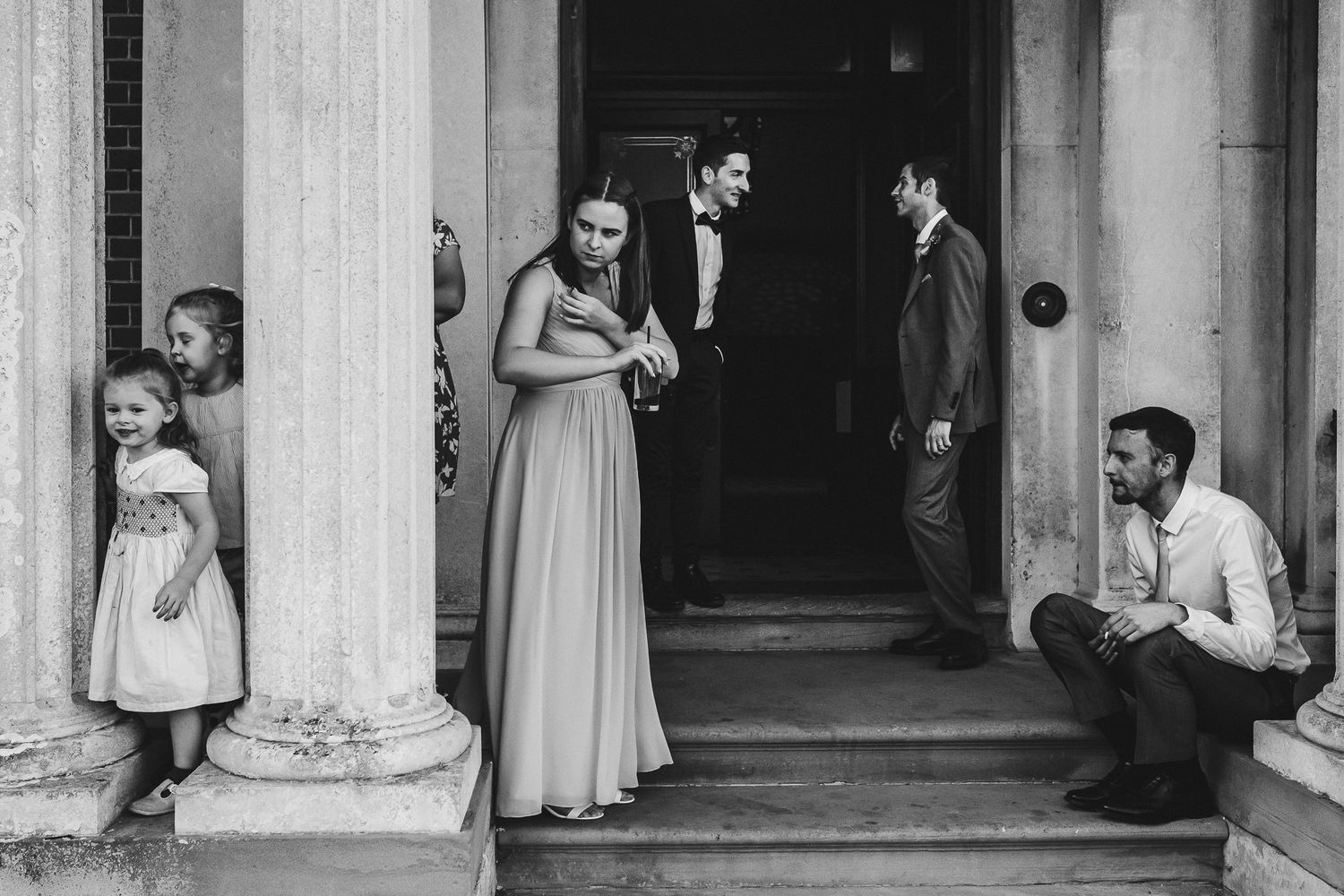 Wedding party members gathered on classic stone steps outside a building entrance.